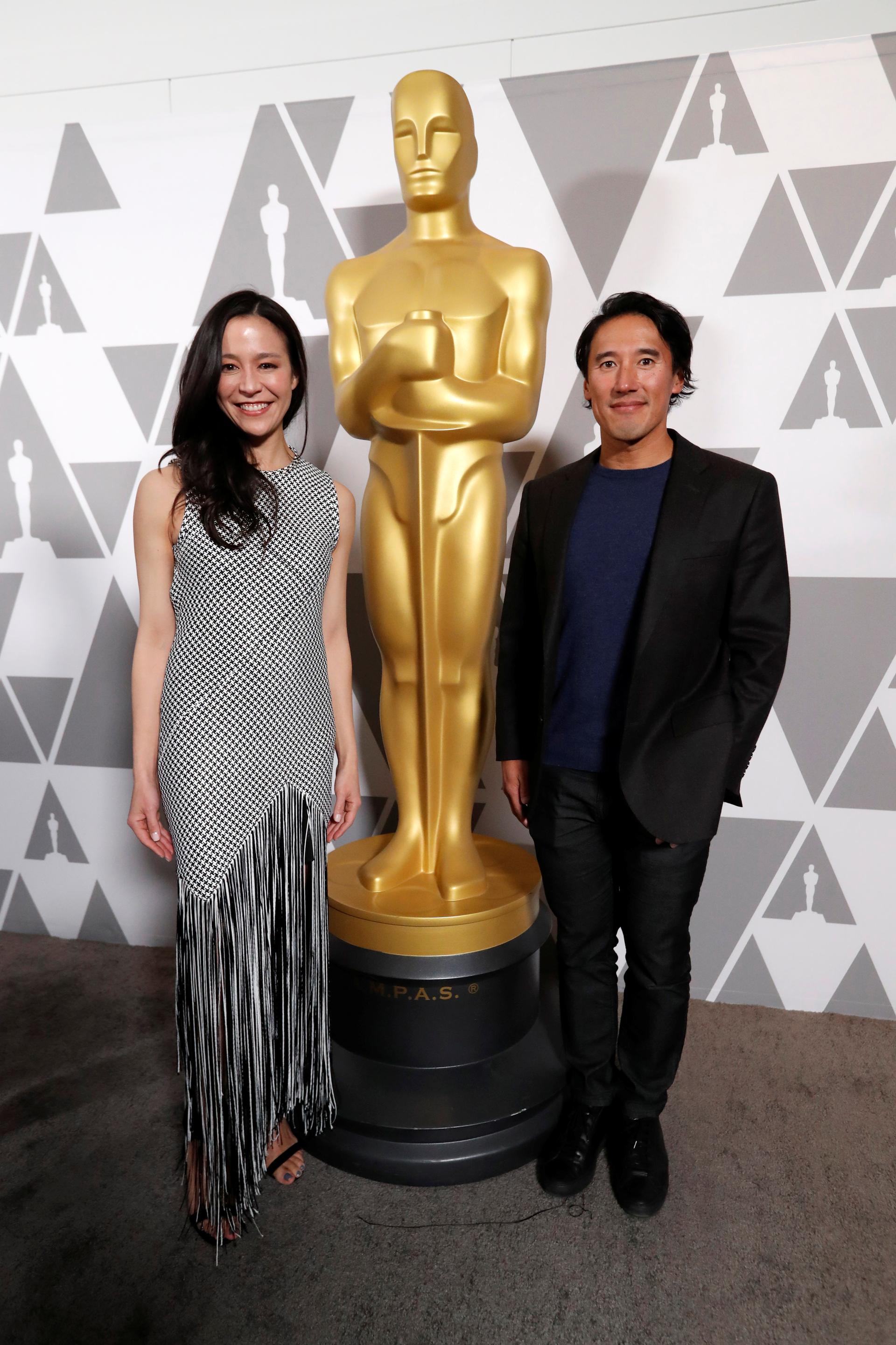 Jimmy Chin and Chai Vasarhalyi stand next to a human size Oscar statue