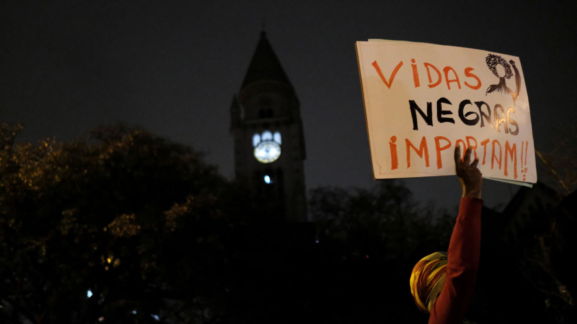 A demonstrator holds a sign reading "Black Lives Matter" in a dark photograph taken in low light.