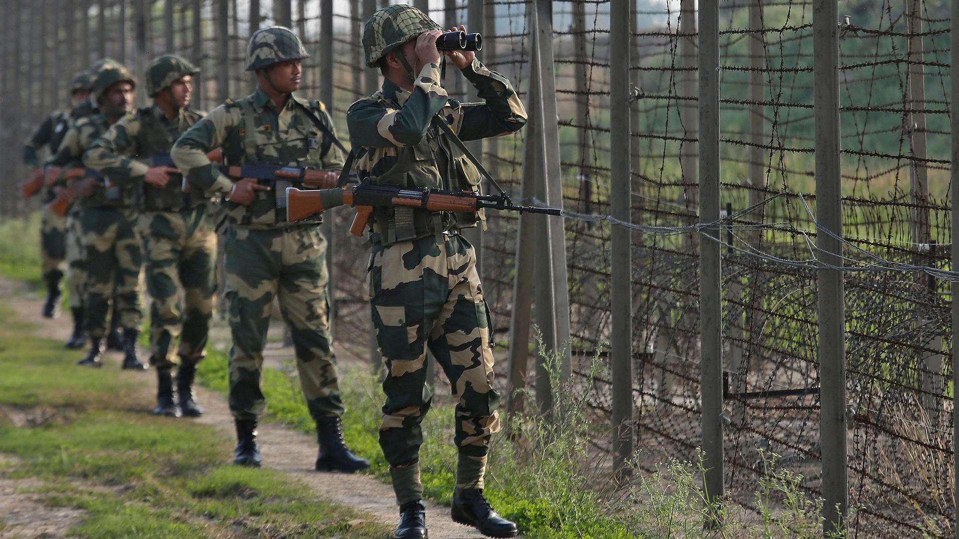 Six of India's Border Security Force soldiers are shown talking along the fenced border in a line.