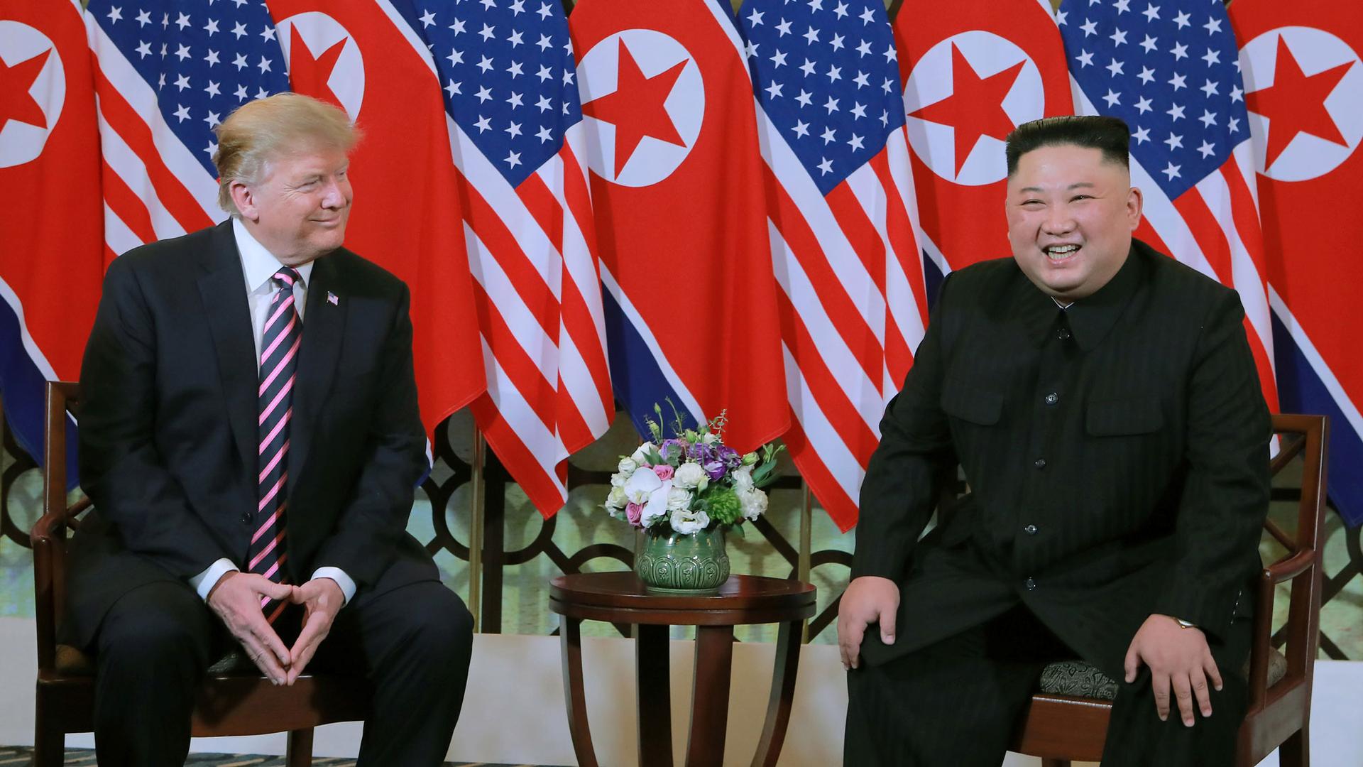 North Korea's leader Kim Jong-un and US President Donald Trump are shown sitting next two each other with US and North Korean flags behind them.