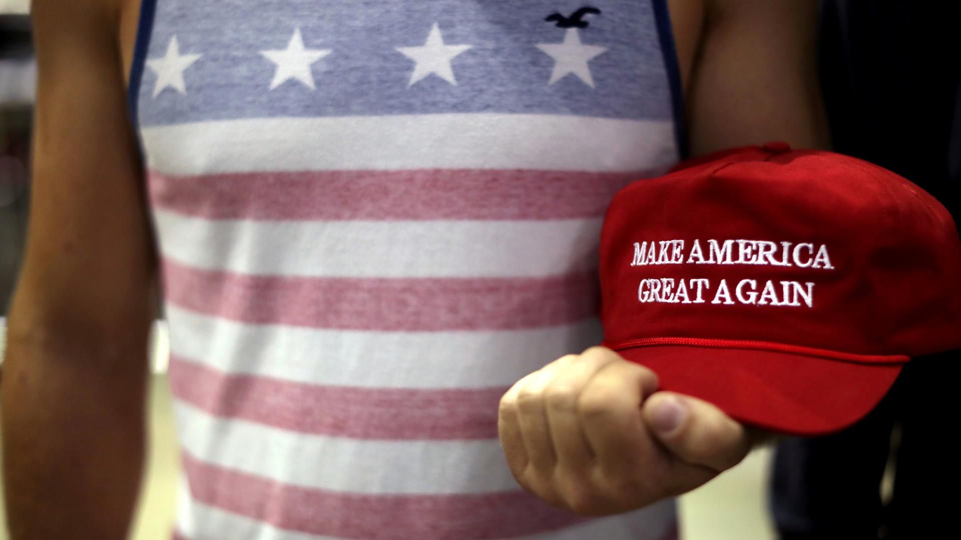 Person holds red MAGA hat in his hand. 