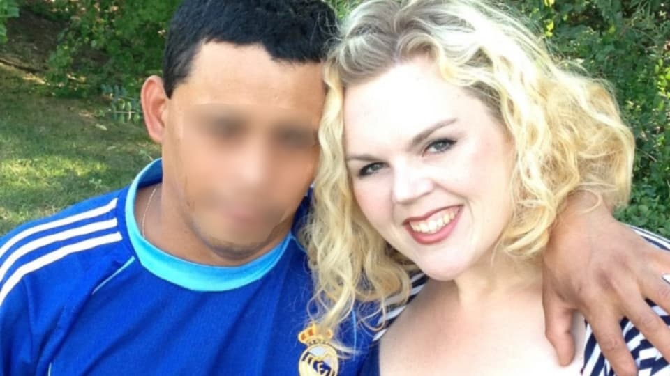 A closeup photo of a blonde woman wearing a blue shirt beside her husband, whose face has been blurred for privacy.