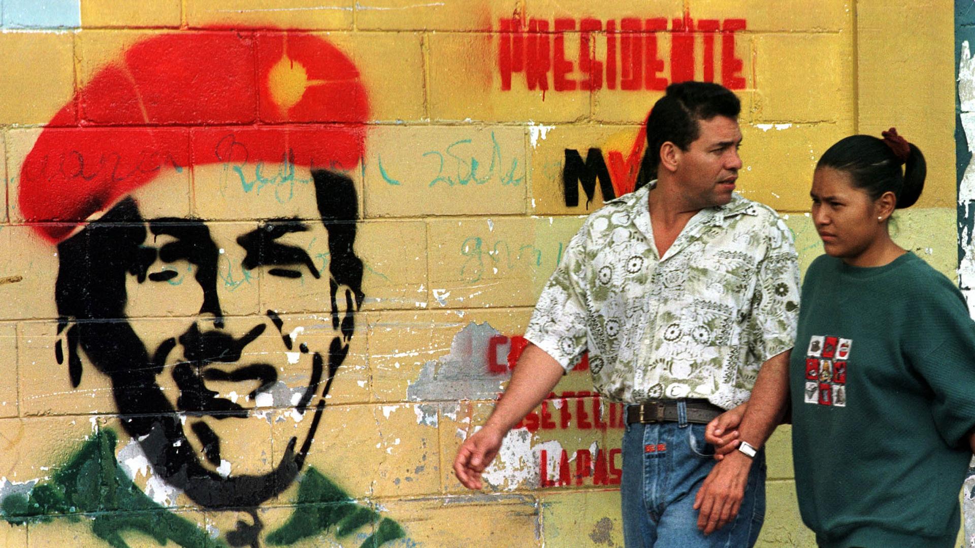 Venezuelans walk past a wall painted with the face of then presidential candidate Hugo Chávez. The leftist military leader tapped into a wave of discontent in the country with falling living standards and corrupt public institutions, December 1998. 