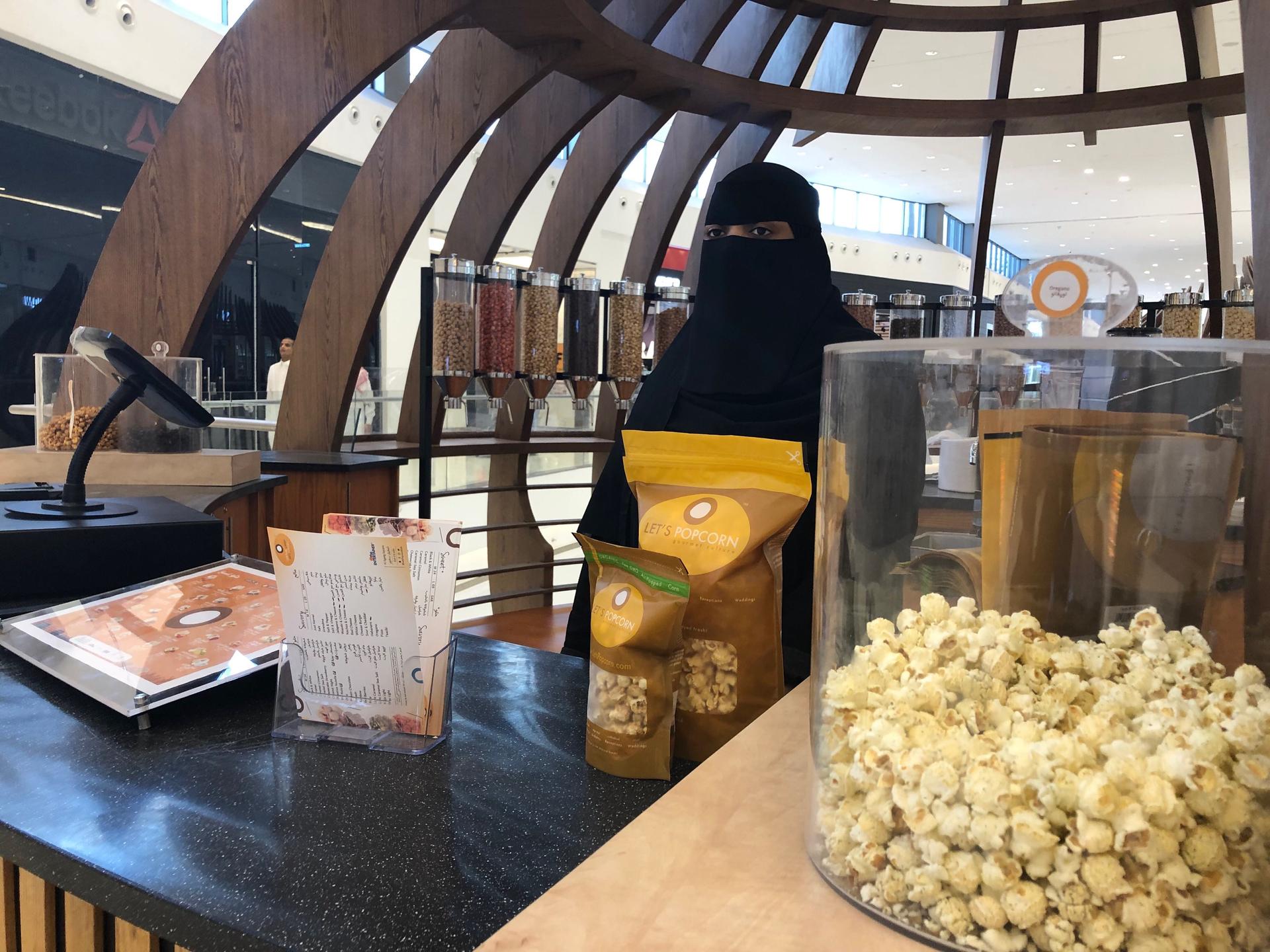 A woman wearing a black veil sells popcorn at a stand at a mall.
