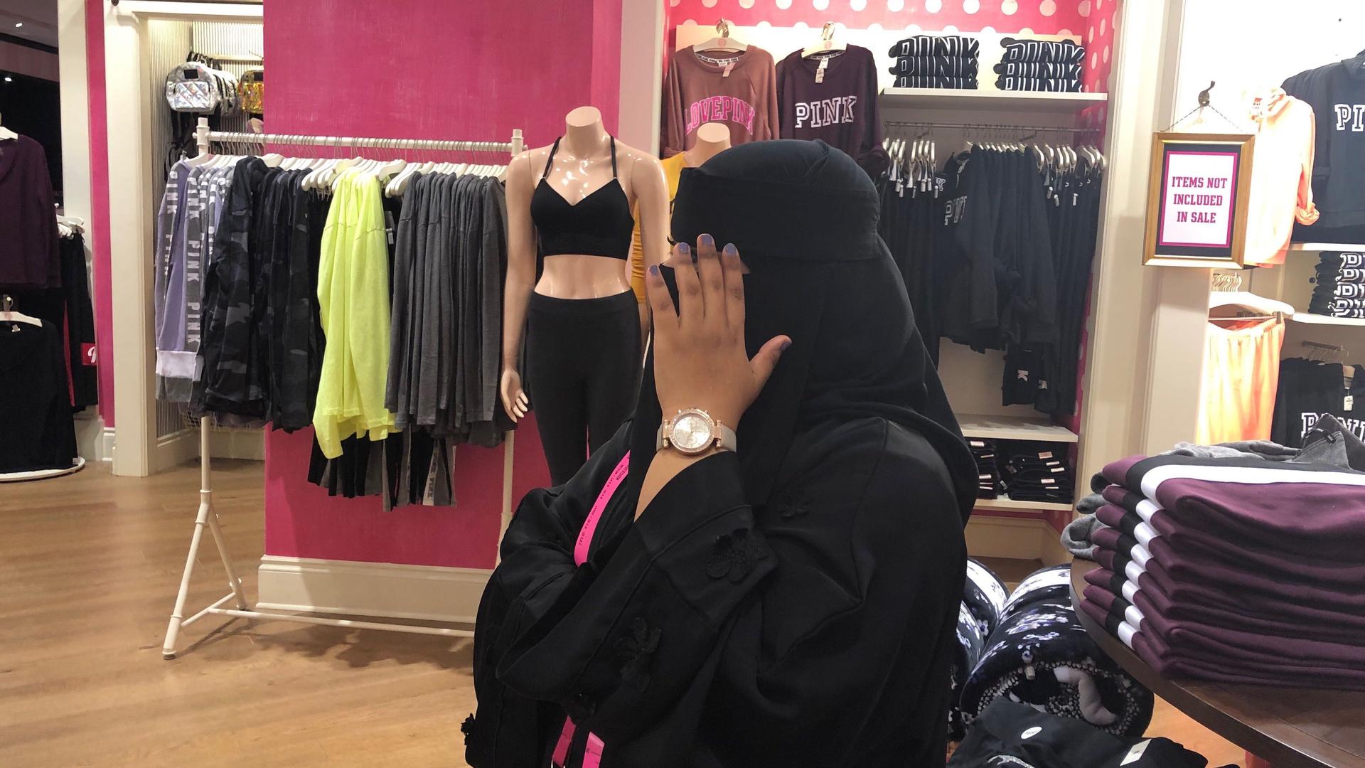A woman wearing a black veil puts her blocks her face standing in a department store. 