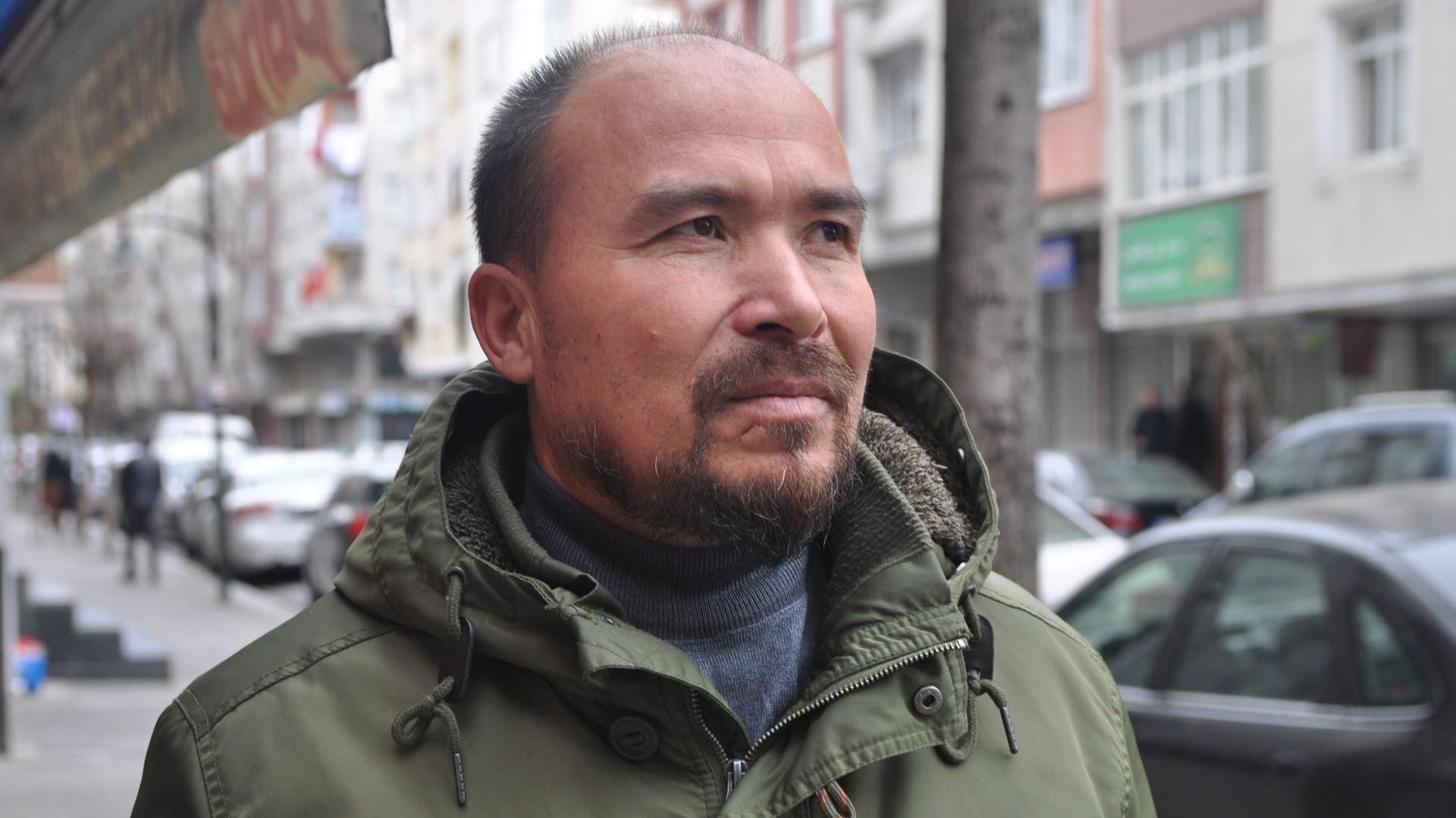 Photo of a bald Uighur man wearing an army-green jacket. 