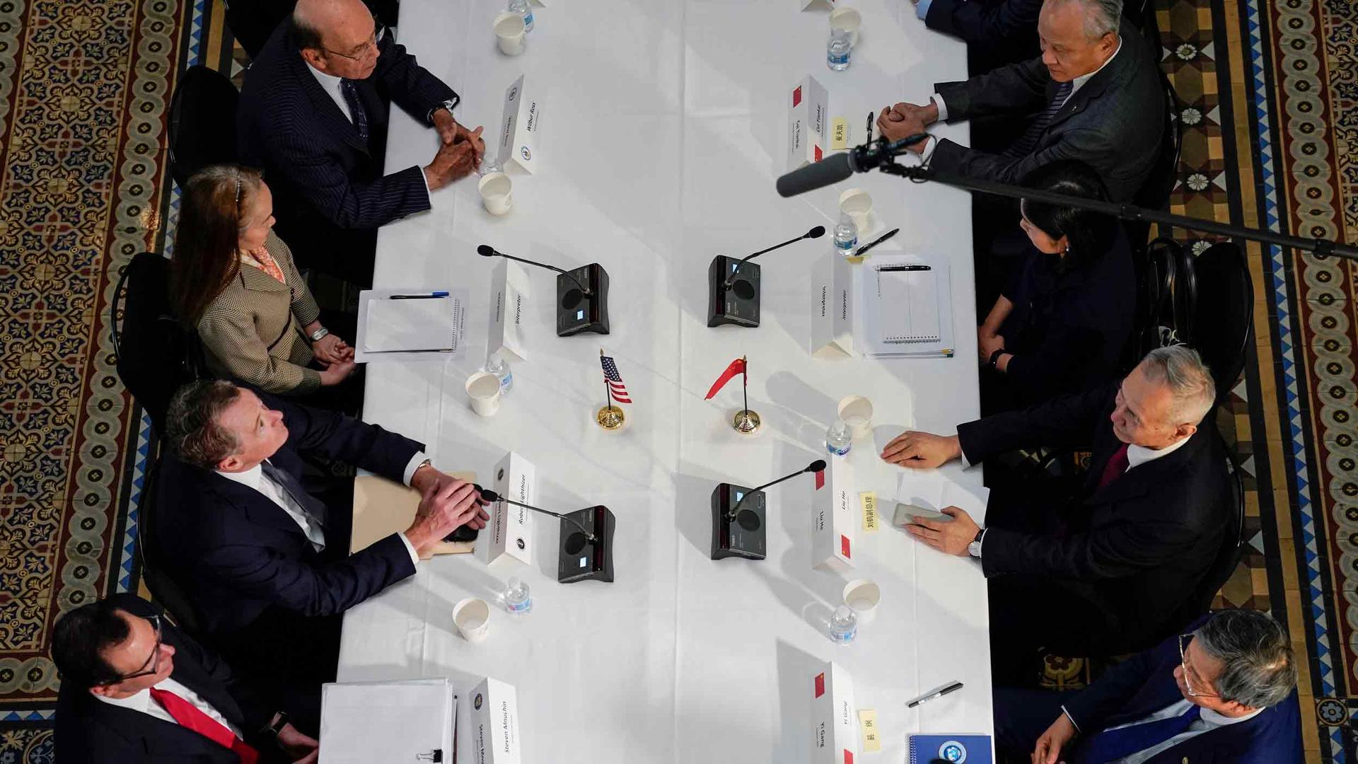 An overhead view of people sitting at a table. In front of each person is a microphone and a name badge.