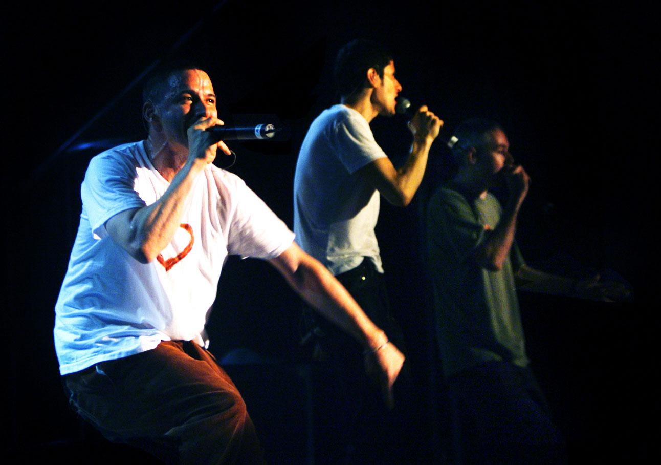 Three men hold microphones and perform on a stage