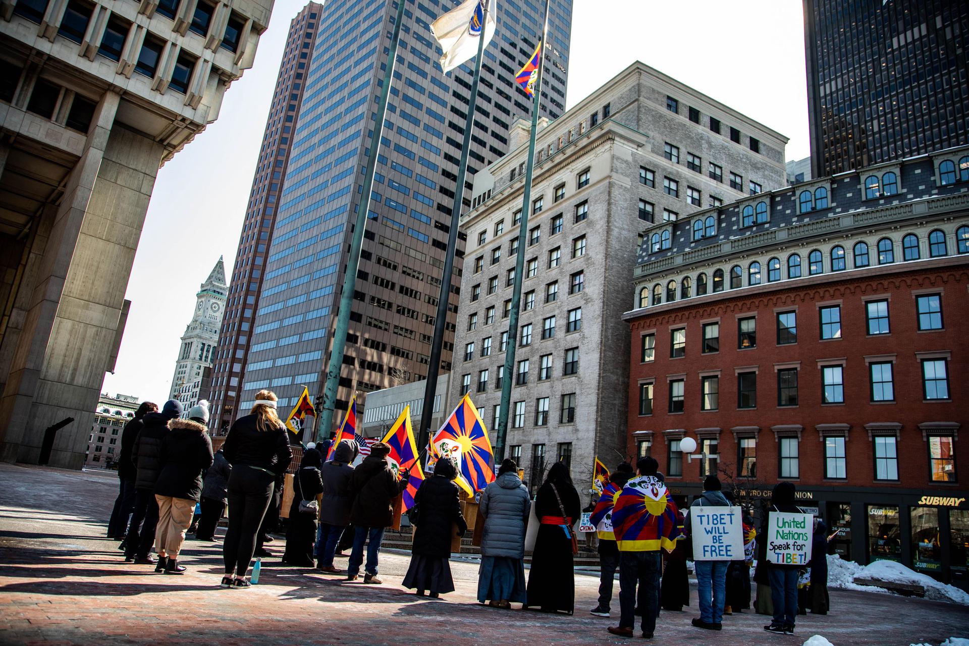 A group of people watch the Tibetan flag on a flagpole surrounded by the historic buildings of downtown Boston