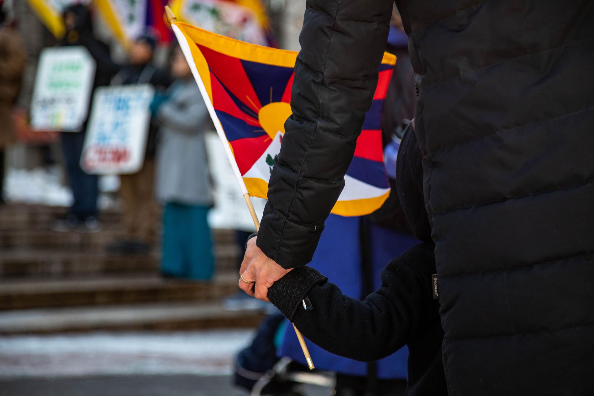 An adult holds a child's hand and a Tibetan flag