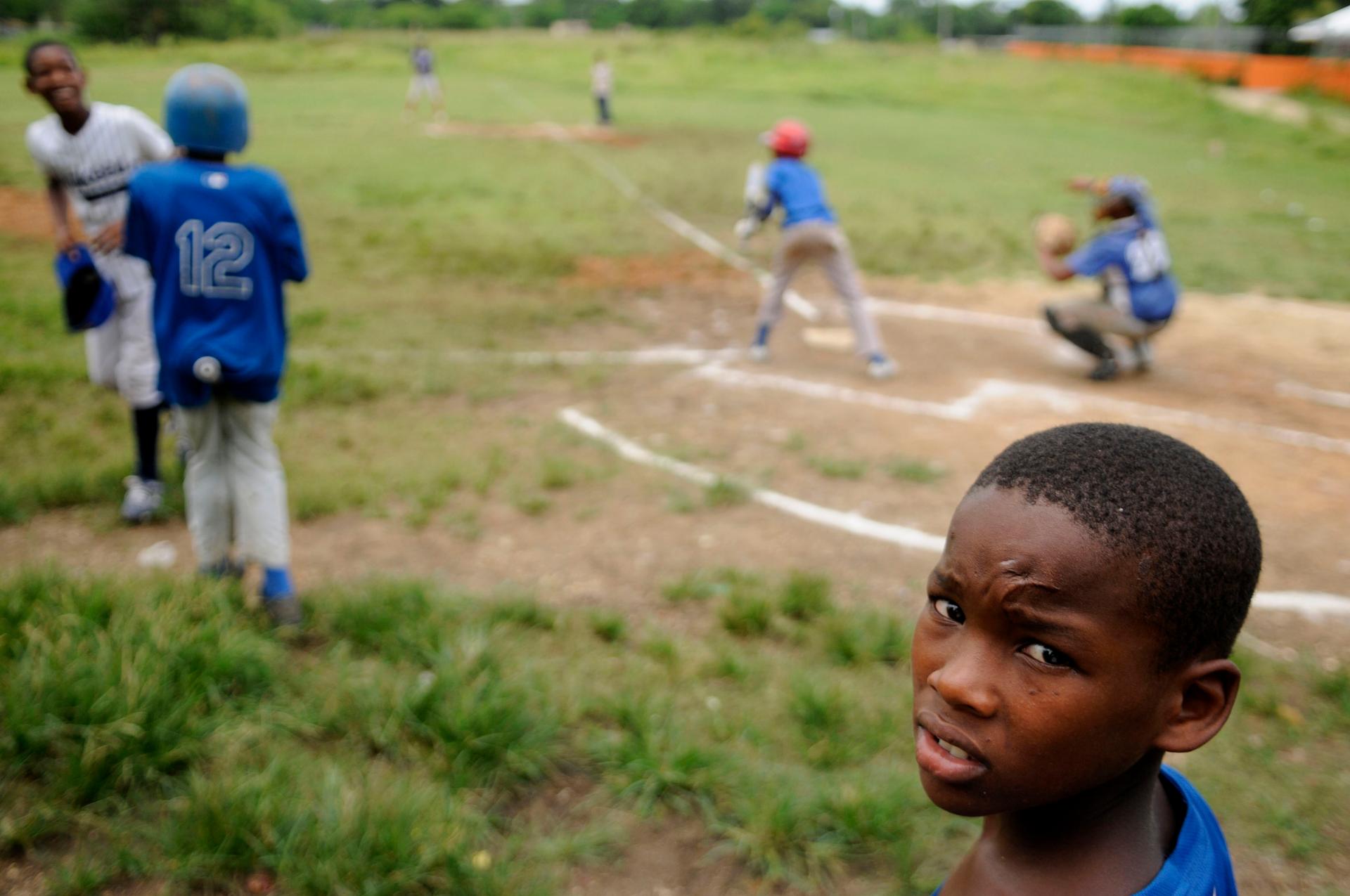 A young boy looks into a camera while others play baseball behind him