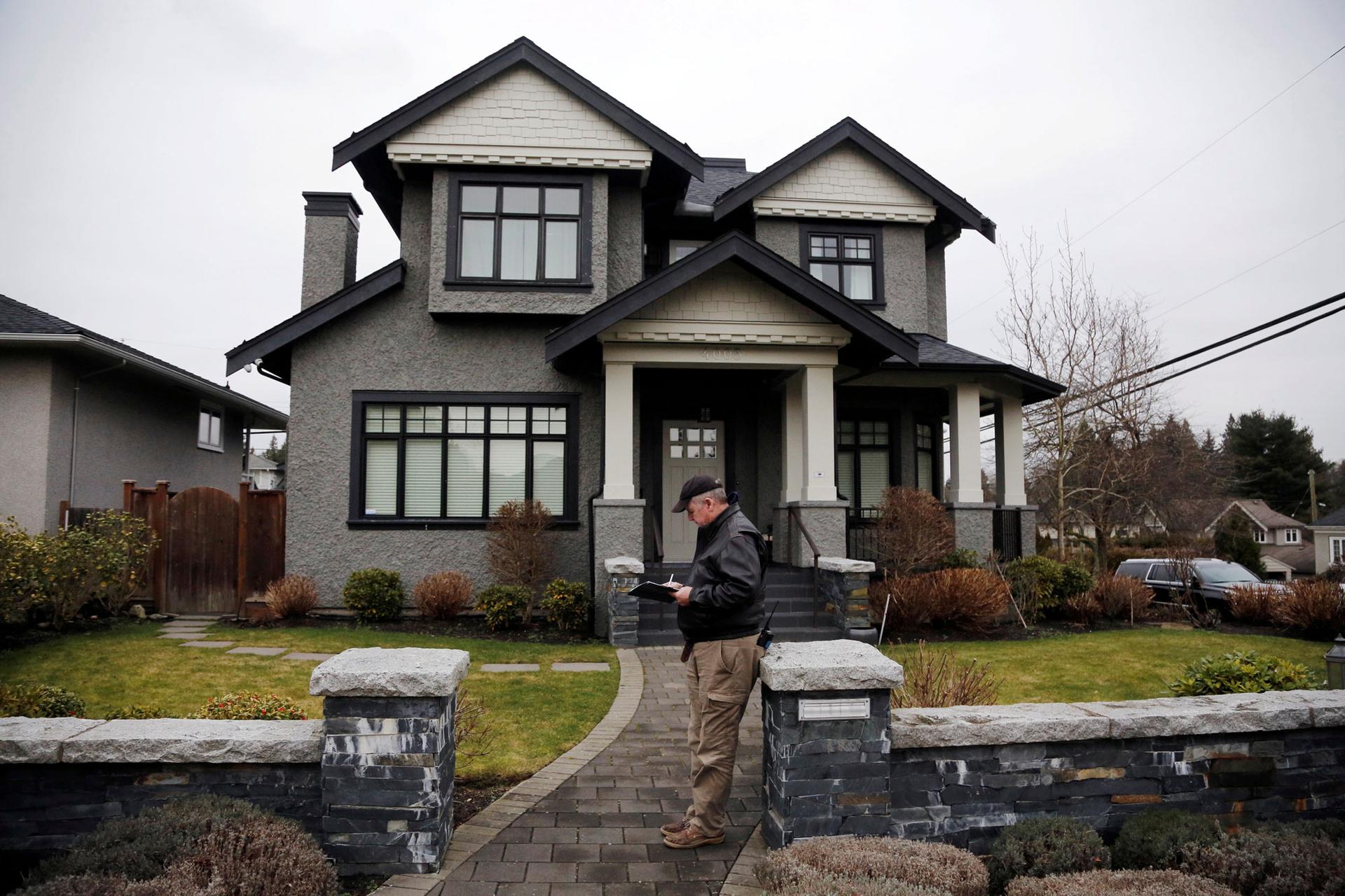 A member of a private security firm is shown stands outside of the family home of Huawei's financial chief Meng Wanzhou with a clipboard and a walkie talkie.