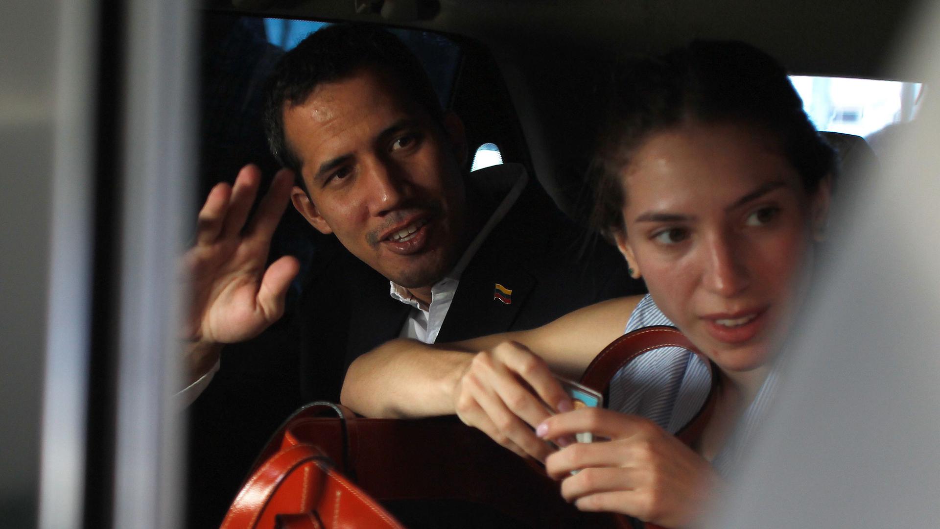 Venezuelan opposition leader Juan Guaidó sits in the back seat of a car next to his wife Fabiana Rosales waving.