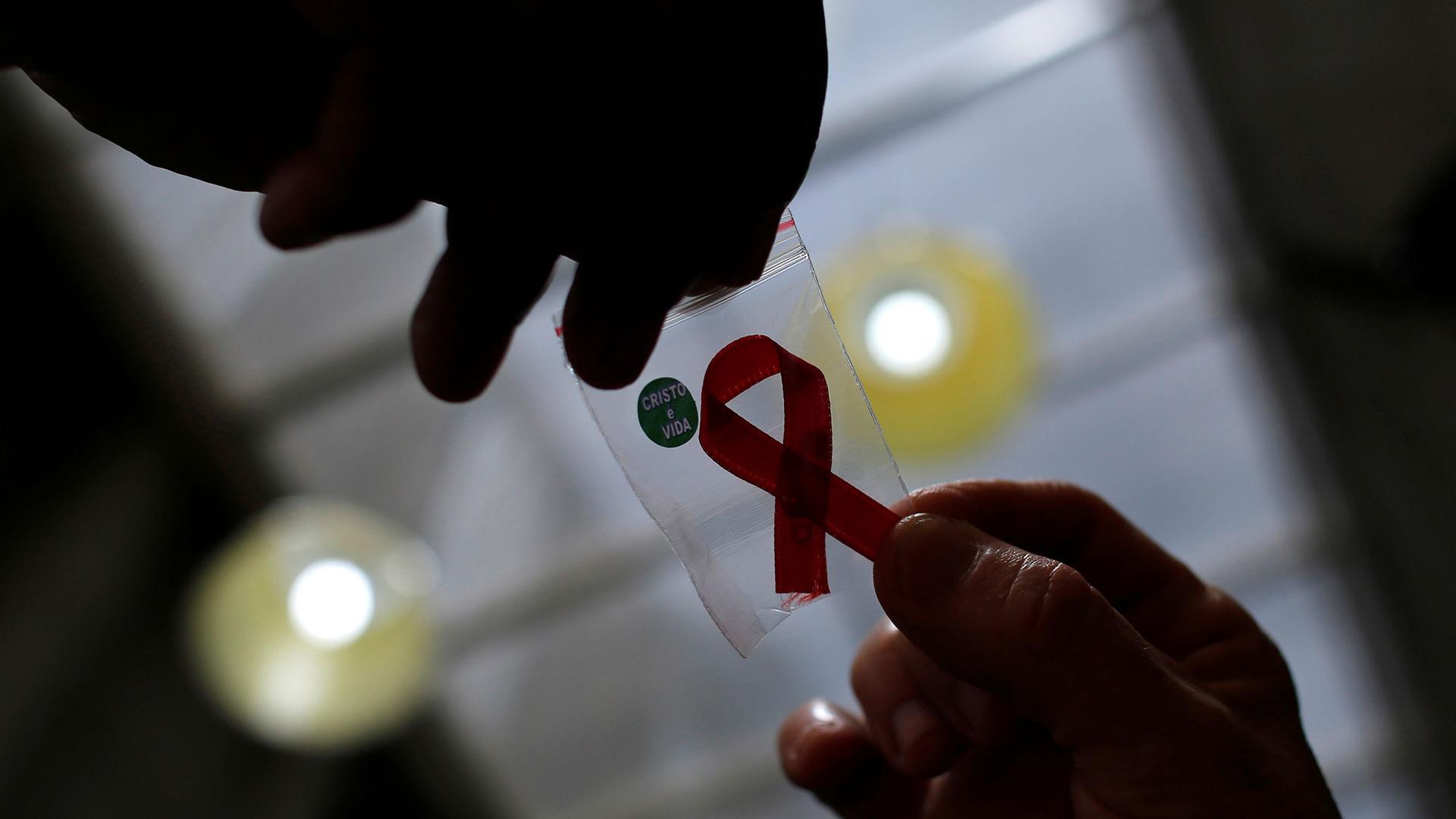 In a picture photographed from underneath, an AIDs ribon is shown in a small plastic baggie in shadow.