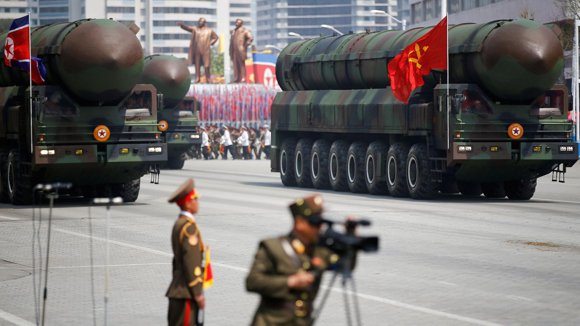 Intercontinental ballistic missiles are shown atop eight-wheeled camoflaged trucks being driven down a street.