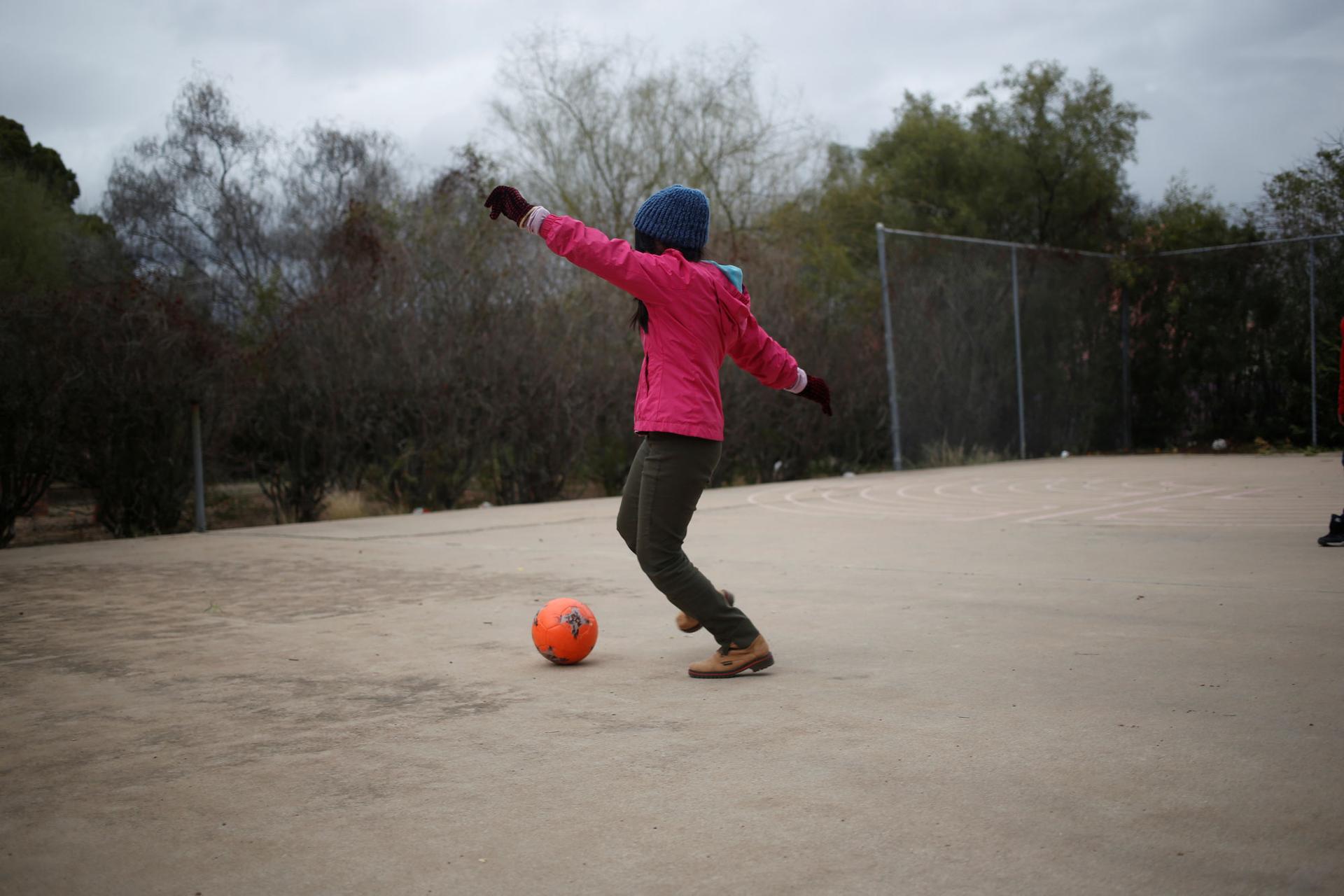 A young girl wearing a pink jacket and wearing a winter hat plays with a ball.