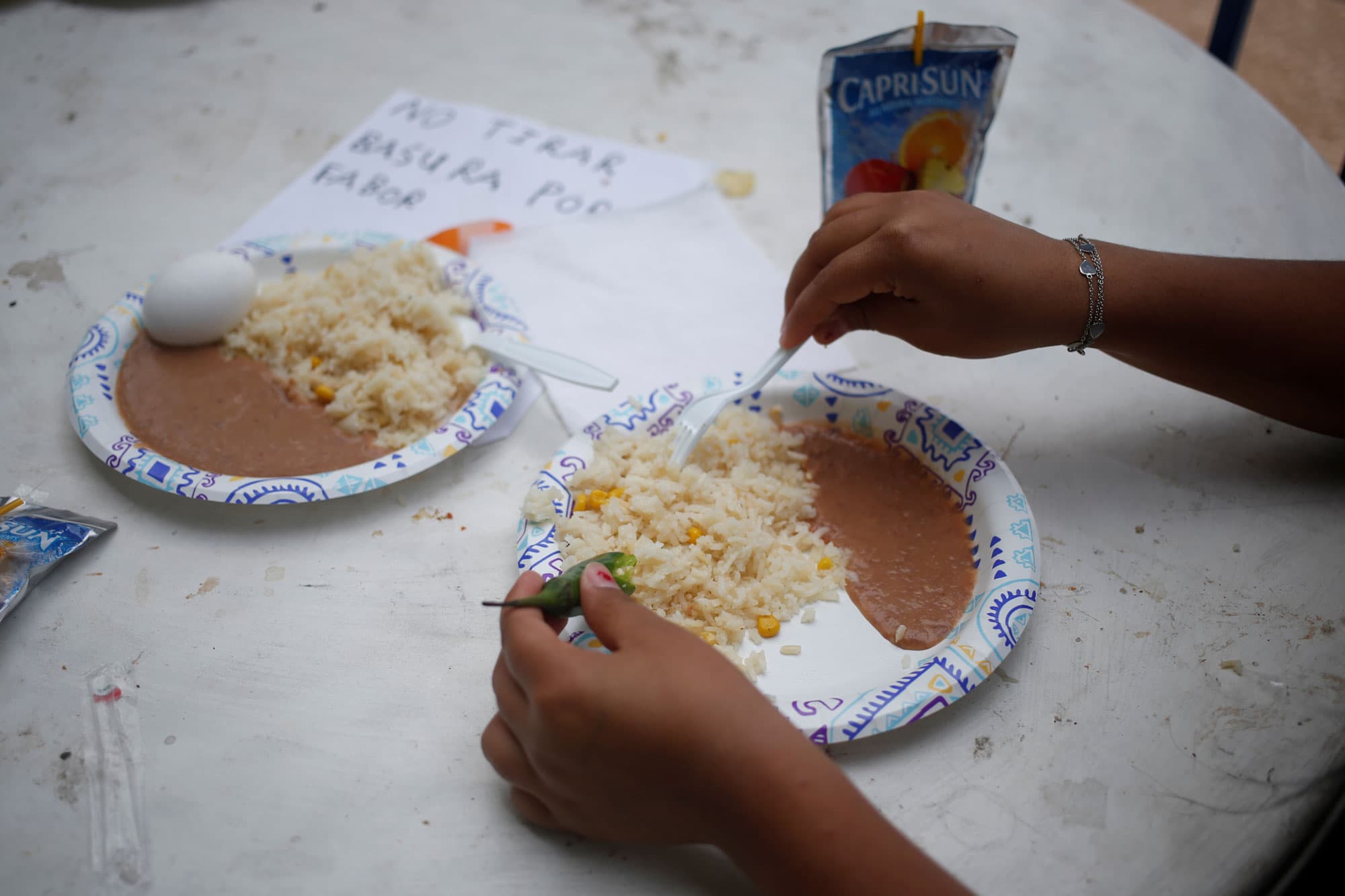 A photograph of a woman's hands and a plate with beans, rice and a jalapeno.
