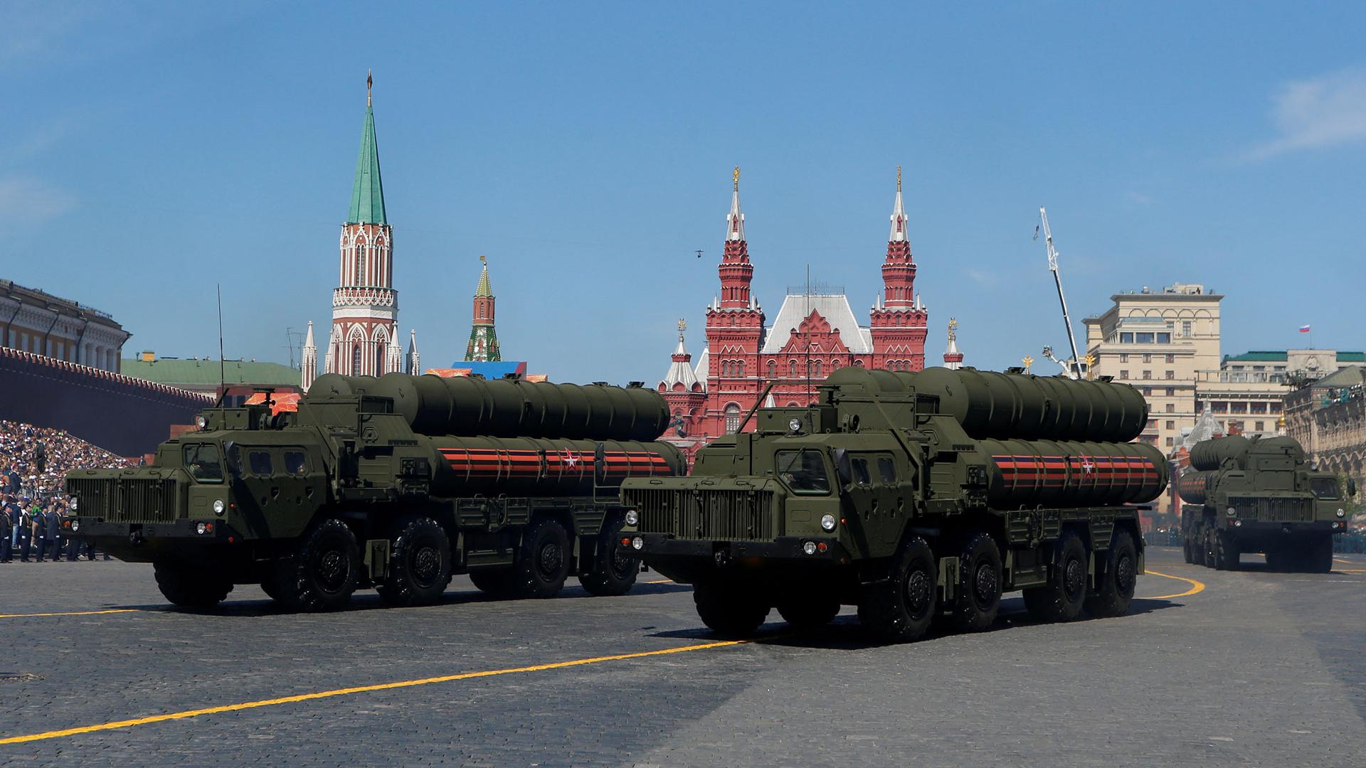 Three large 8-wheeled trucks carrying air defense systems are shown driving down a street.