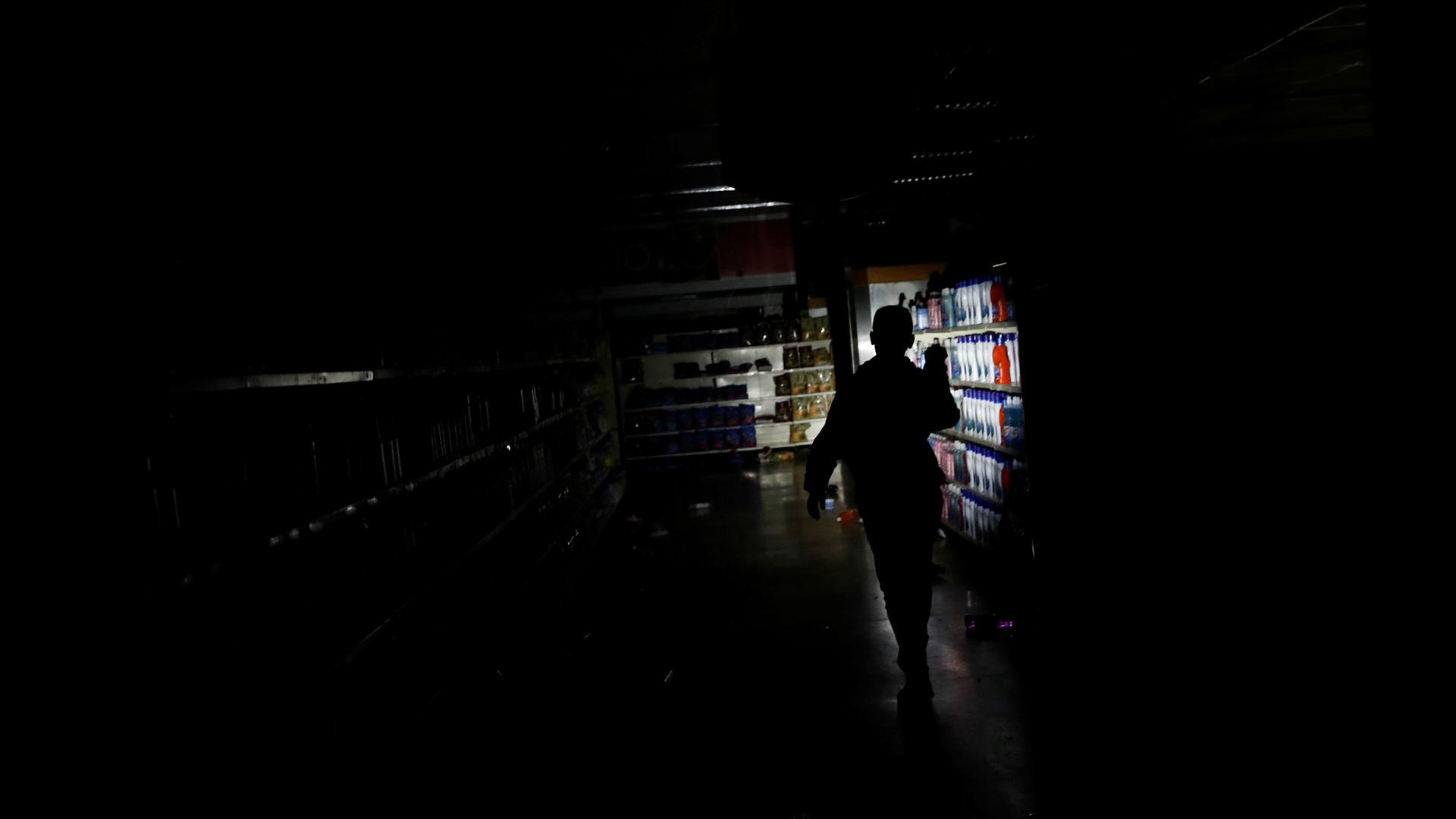 A darkened supermarket is show with one lone flashlight being used by a worker.