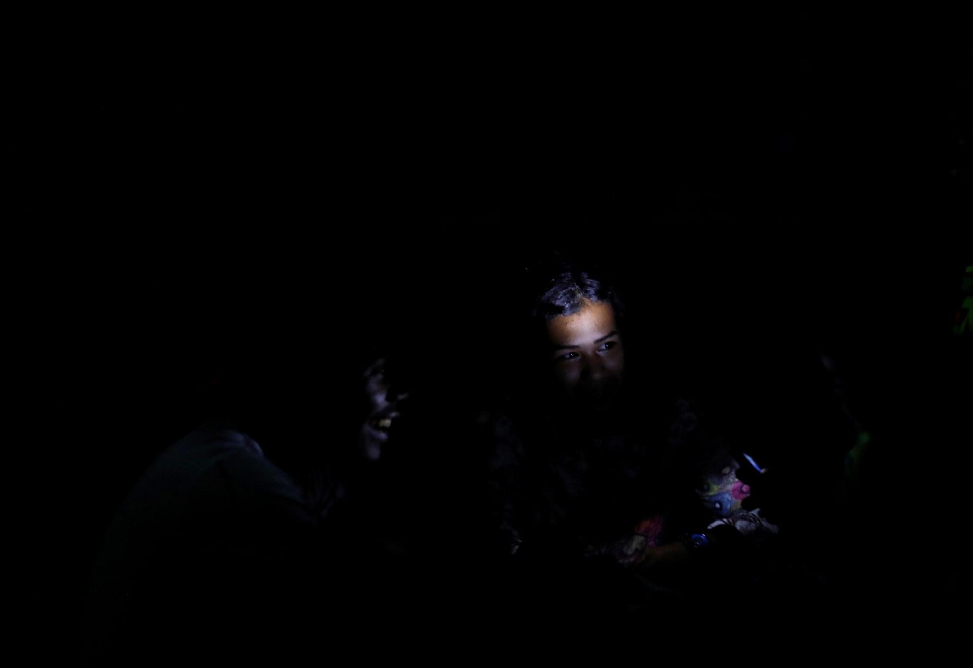In a nearly all dark photograph, a child's face is illuminated by a cellphone light.