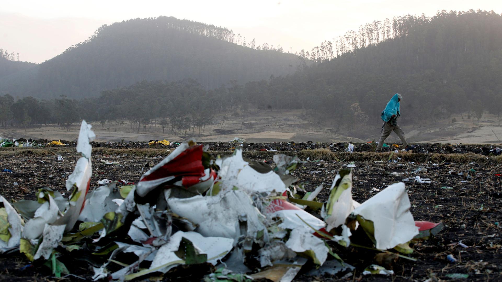 Debris from the Ethiopian Airlines Flight ET 302 plane crash is seen in the near ground of the photo with a man walking past in the background.