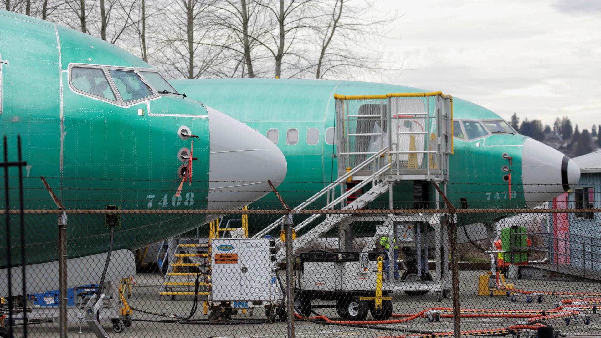 The front end of two Boeing 737 MAX 8 aircraft with a green body and white nose, are parked at a Boeing production facility.