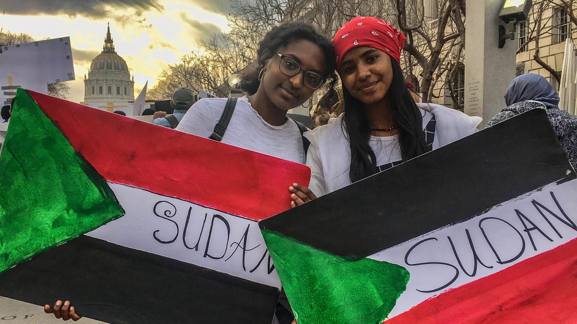 Two young women hold Sudanese flag posters.