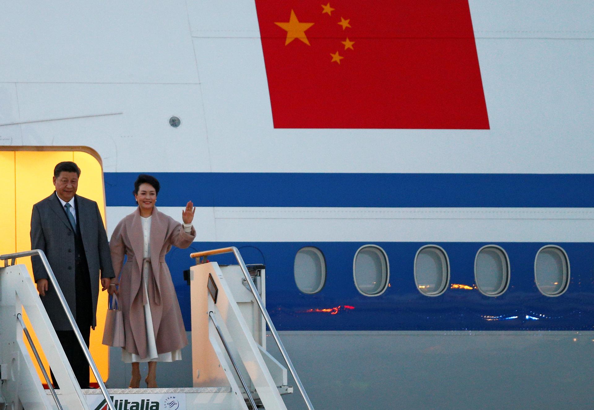 Xi Jinping and his wife step down from an airplane and wave.