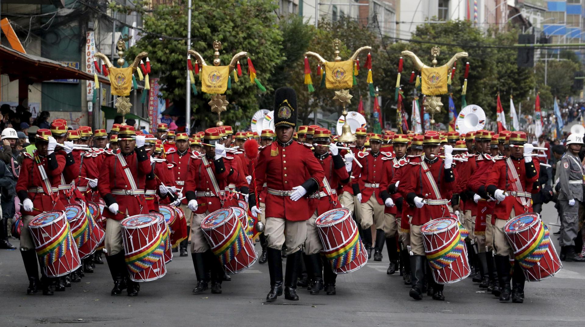 a string of men in red uniforms march with drums