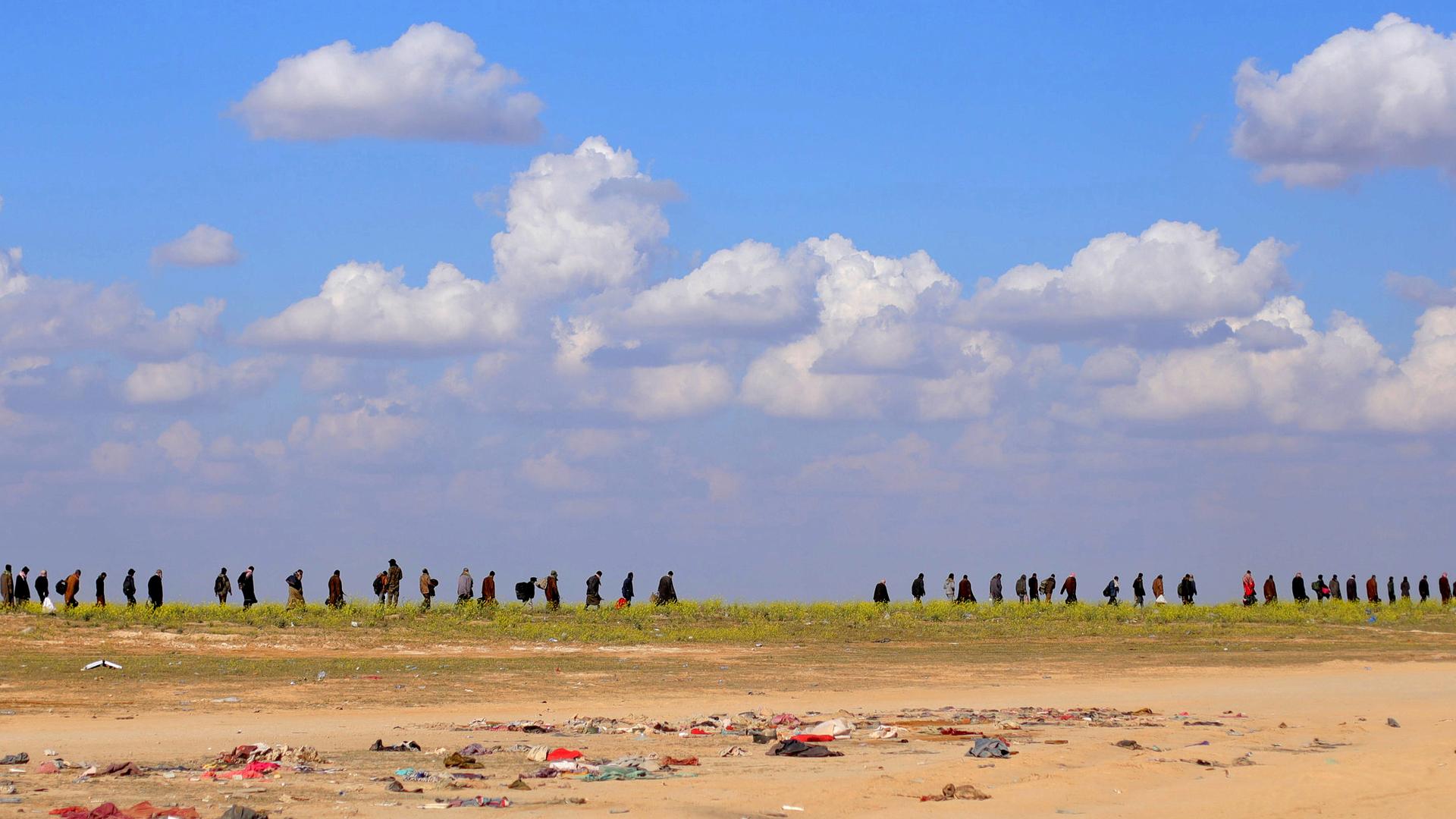 Civilians walk in a line in the desert. 