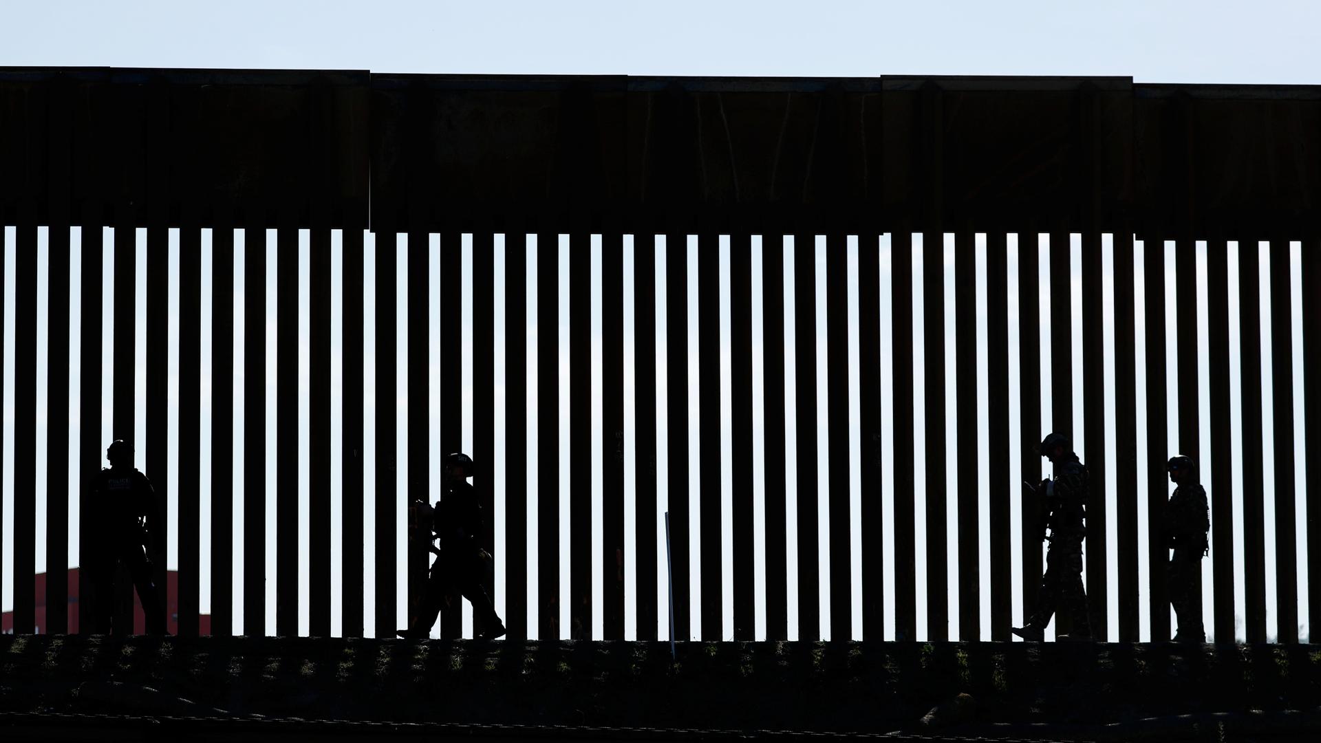 Shadow of patrolmen along slated wall at US border. 