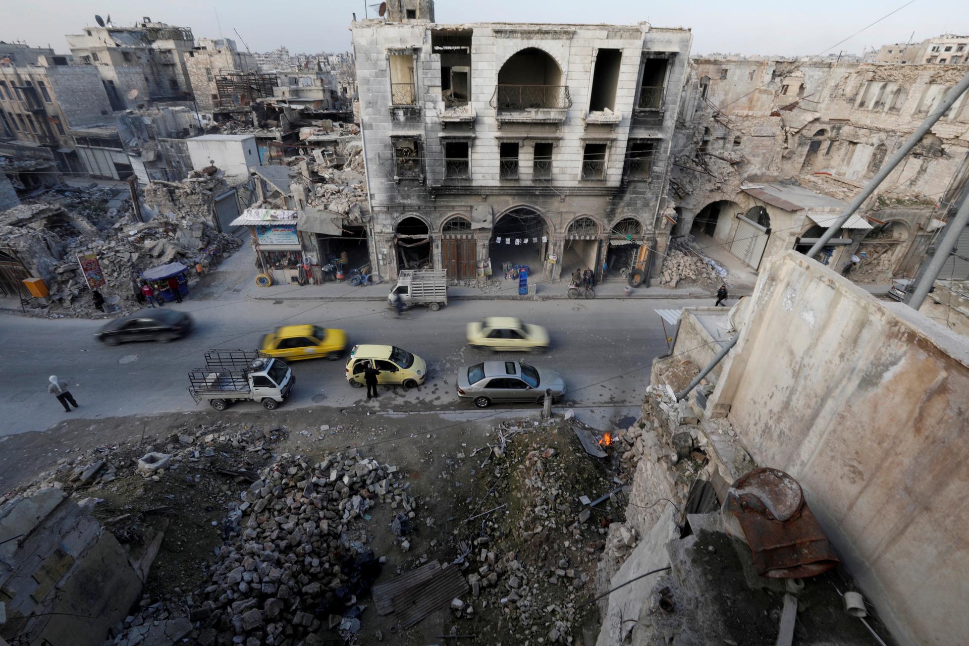 Destroyed buildings, cars, and people and are seen from across the street in Aleppo's old town. 