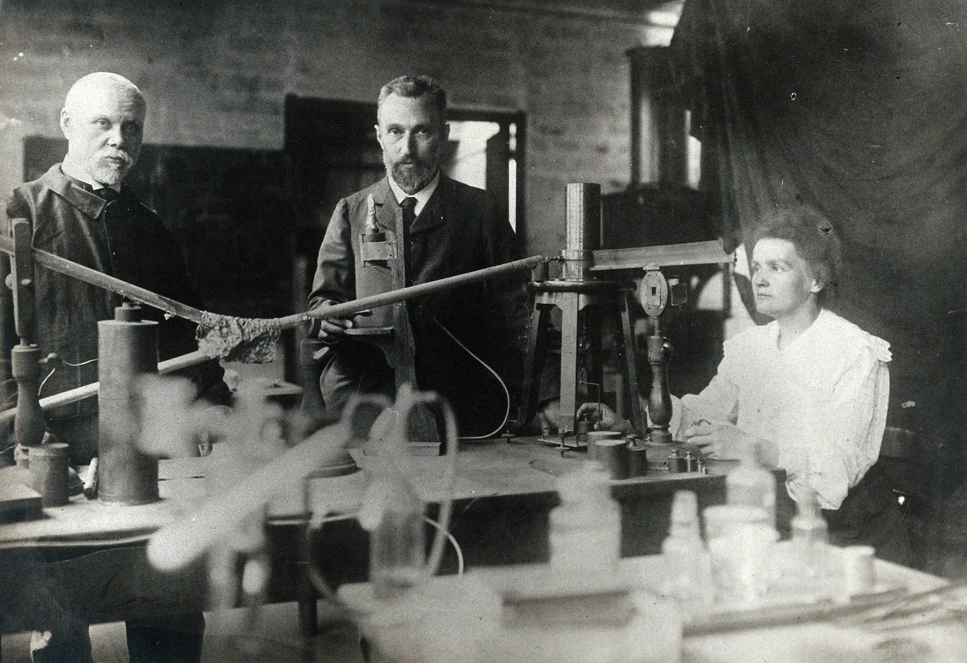 A black and white photo showing three scientists in an old looking laboratory.