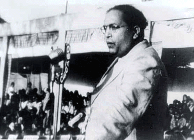 A black and white photo of a man in a suit speaking into a microphone in a crowd