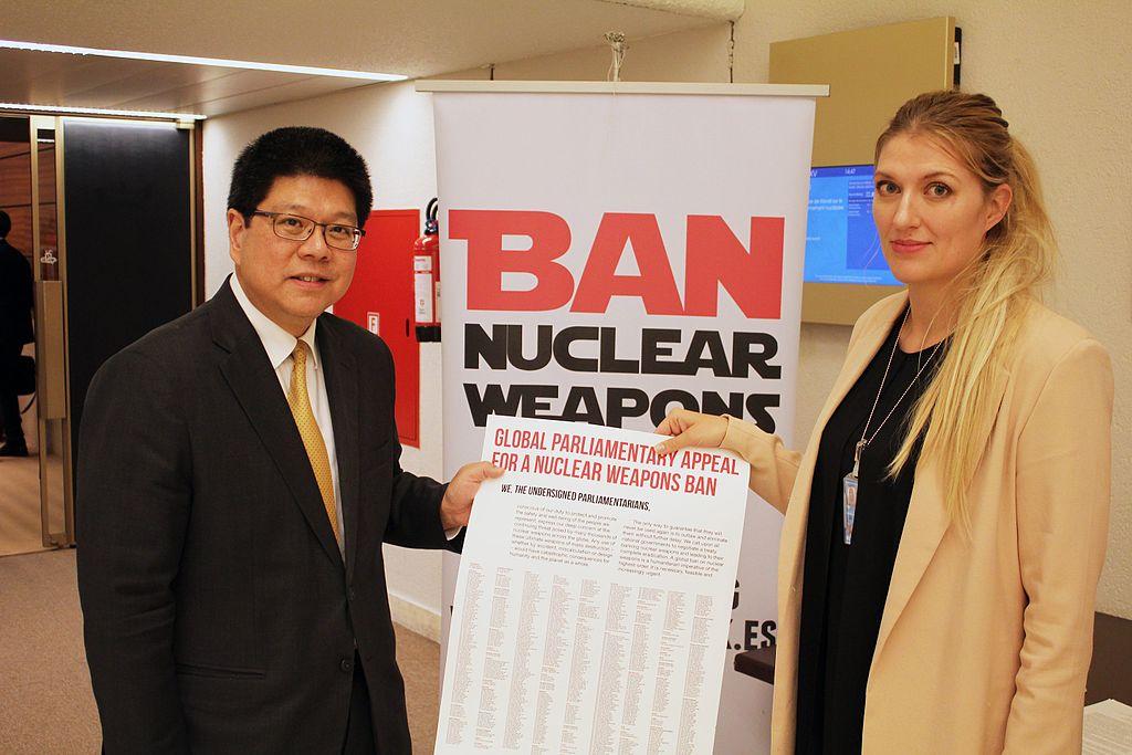 Two diplomats stand in front of a sign that reads ban nuclear weapons