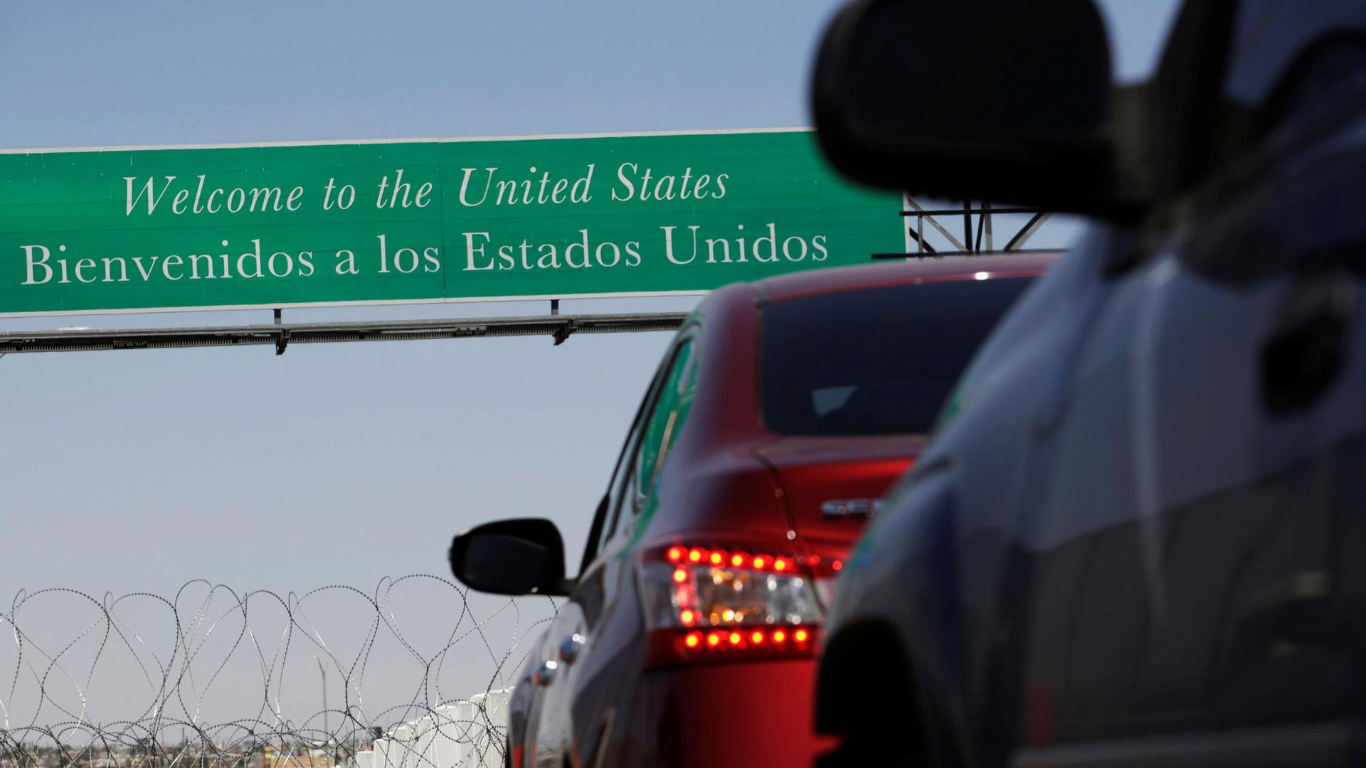 A sign says "Welcome to the United States" as cars line up underneath it
