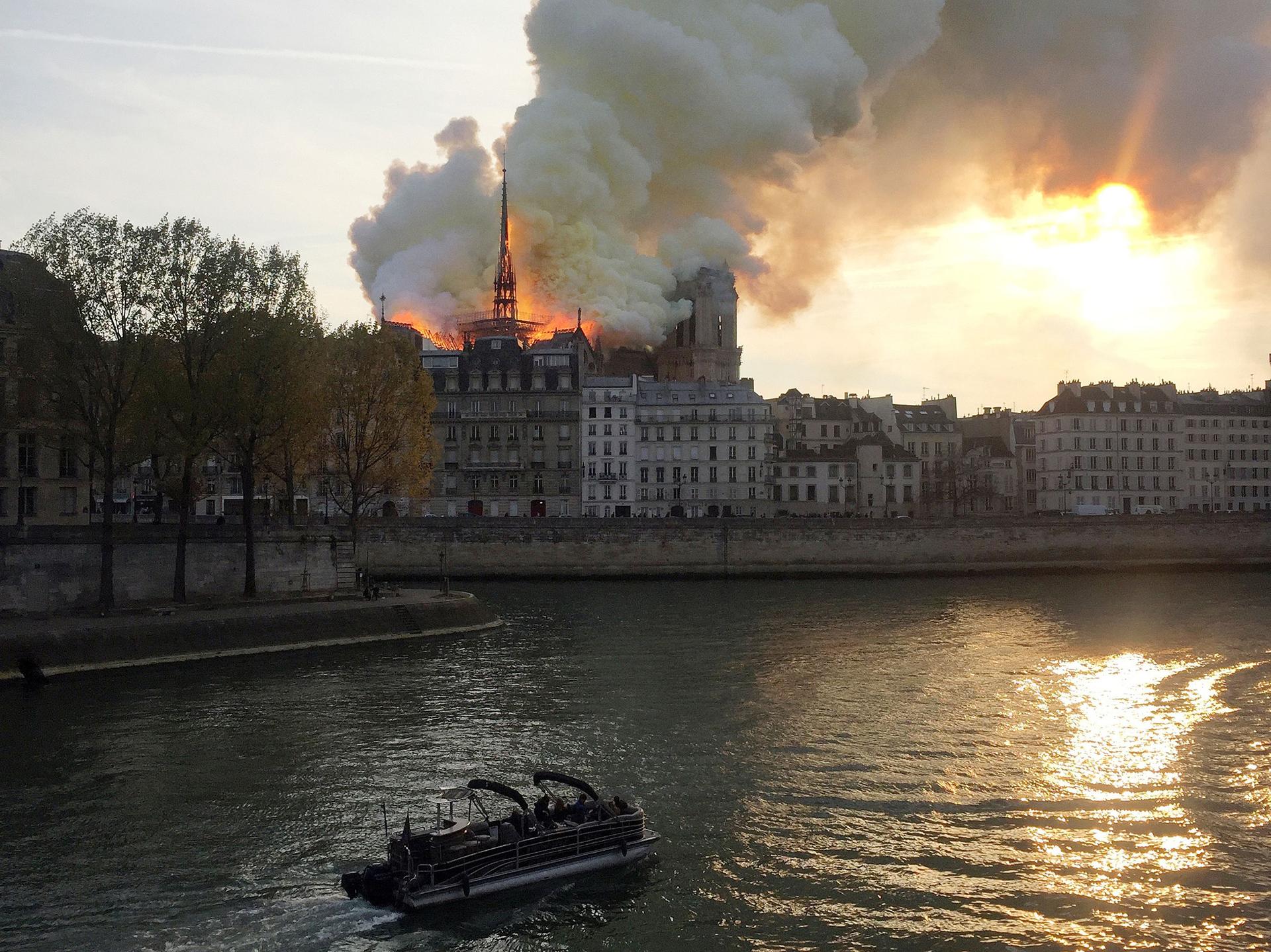 White smoke billows from the top of Notre Dame, see over the river Seine while a boat passes by