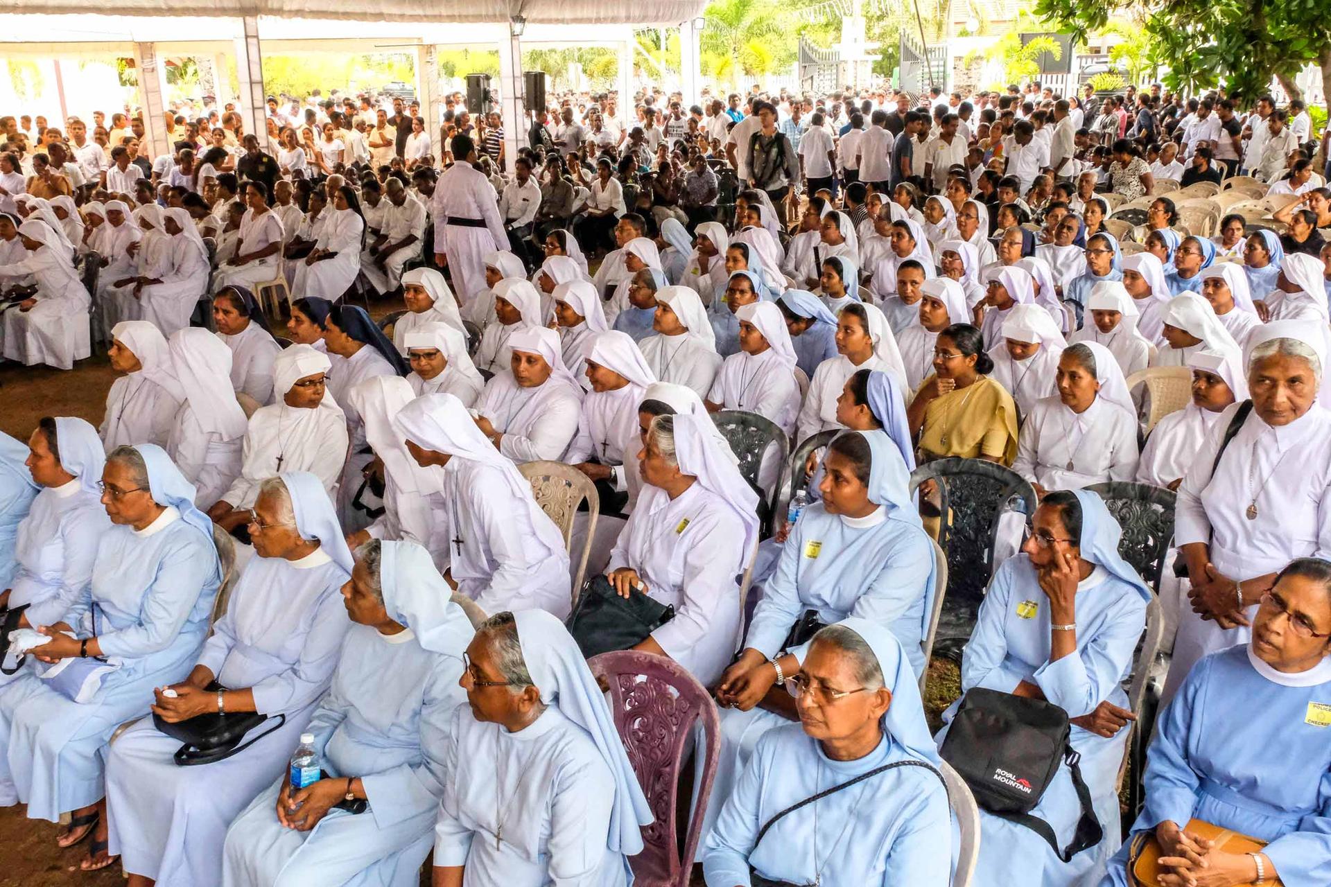 Nuns and other worshippers sit under a large tent