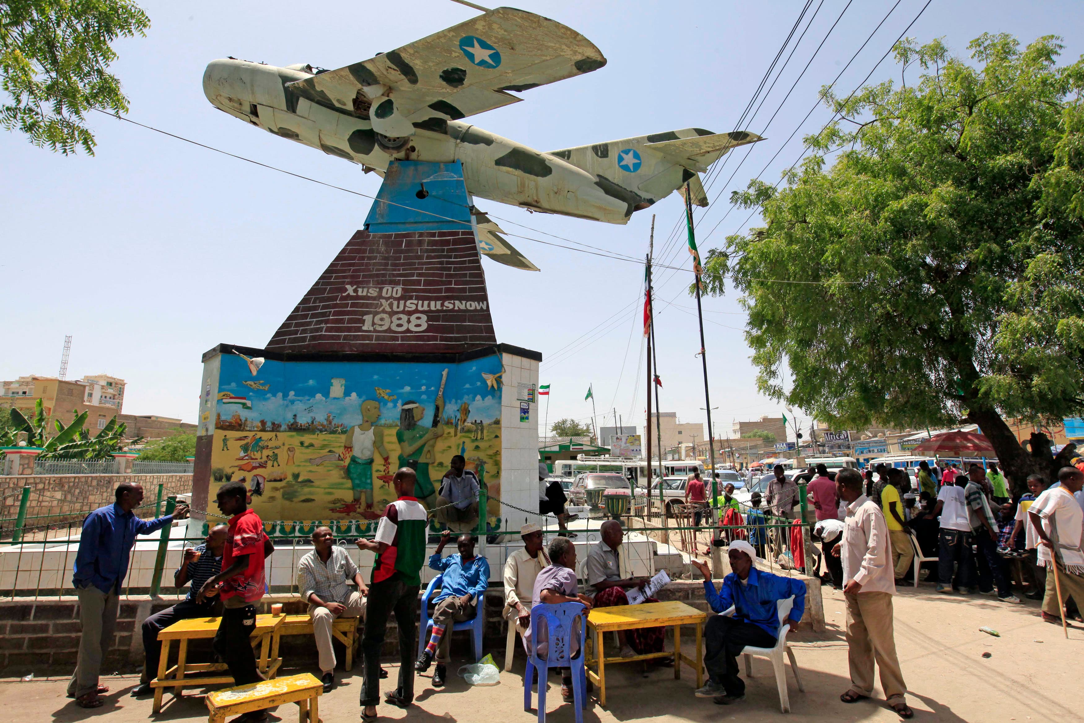 People stand underneath a war memorial in shape of airplane.