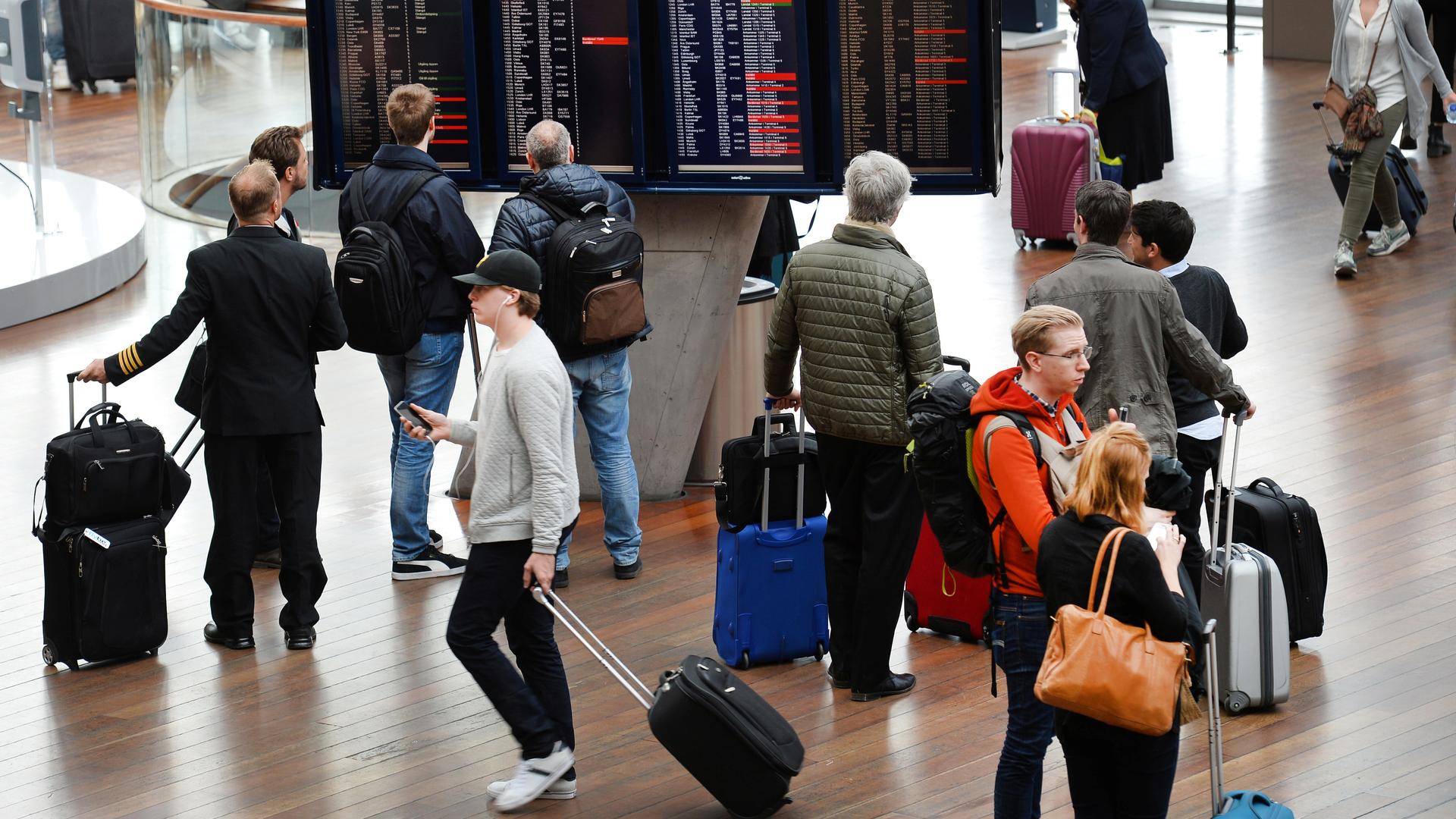 Travelers with roller bags walk and look at departure screens