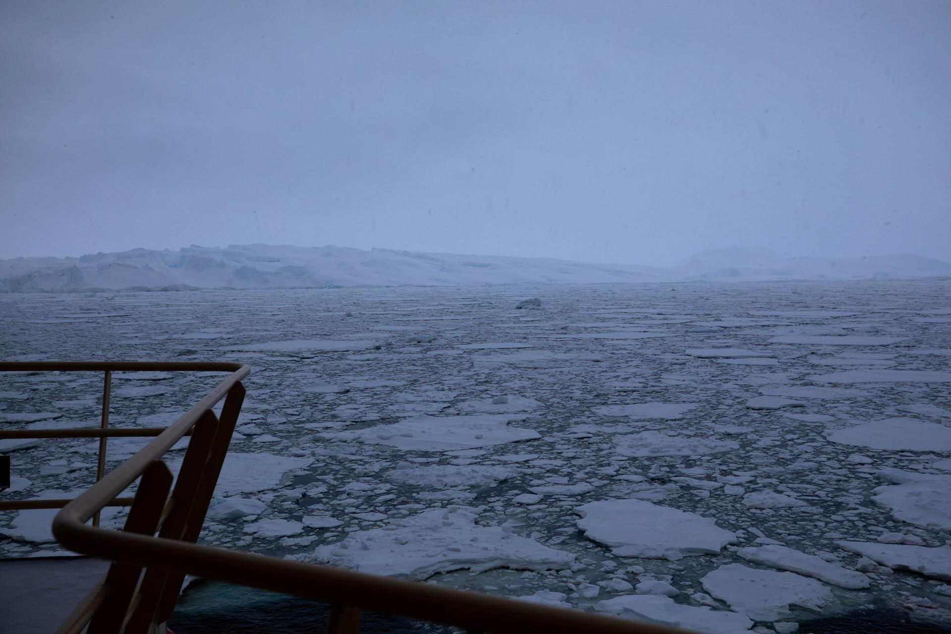 The brown railing of the research vessel is shown in the near ground with larger pancake ice formations in the Amundsen Sea.