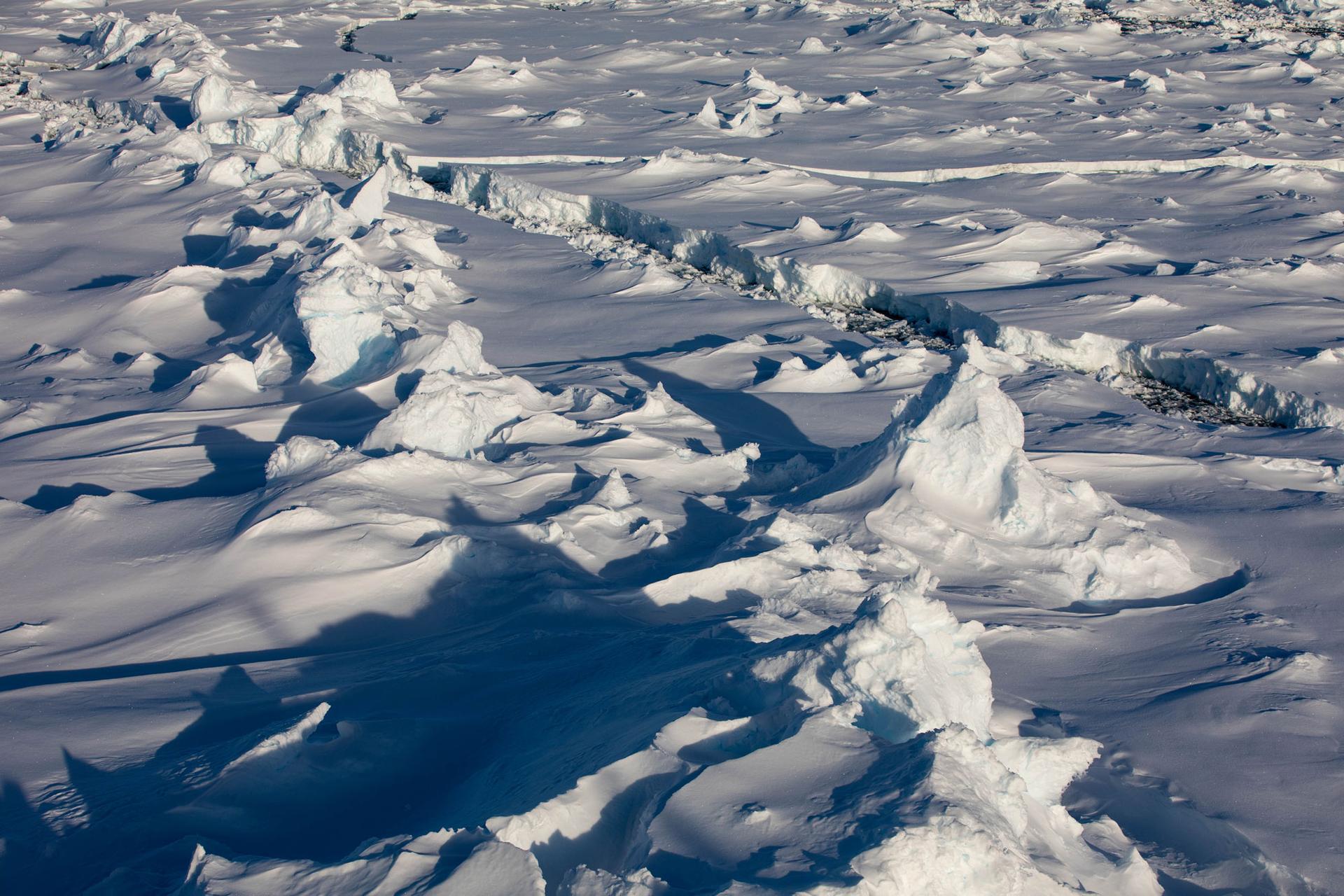 As it ages, large white pieces of ice crash into each other to form pressure ridges in a photo with a thin water path through the two sides.