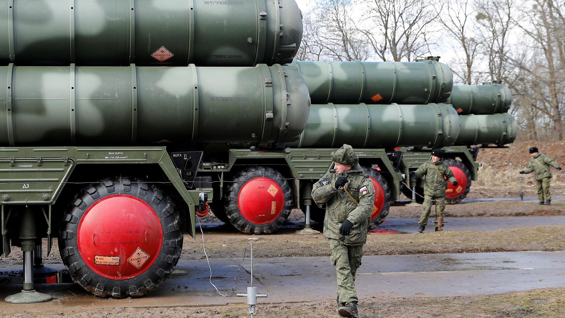 Russian servicemen dressed in fatigues stand next to a large trucks with surface-to-air missile system on top.