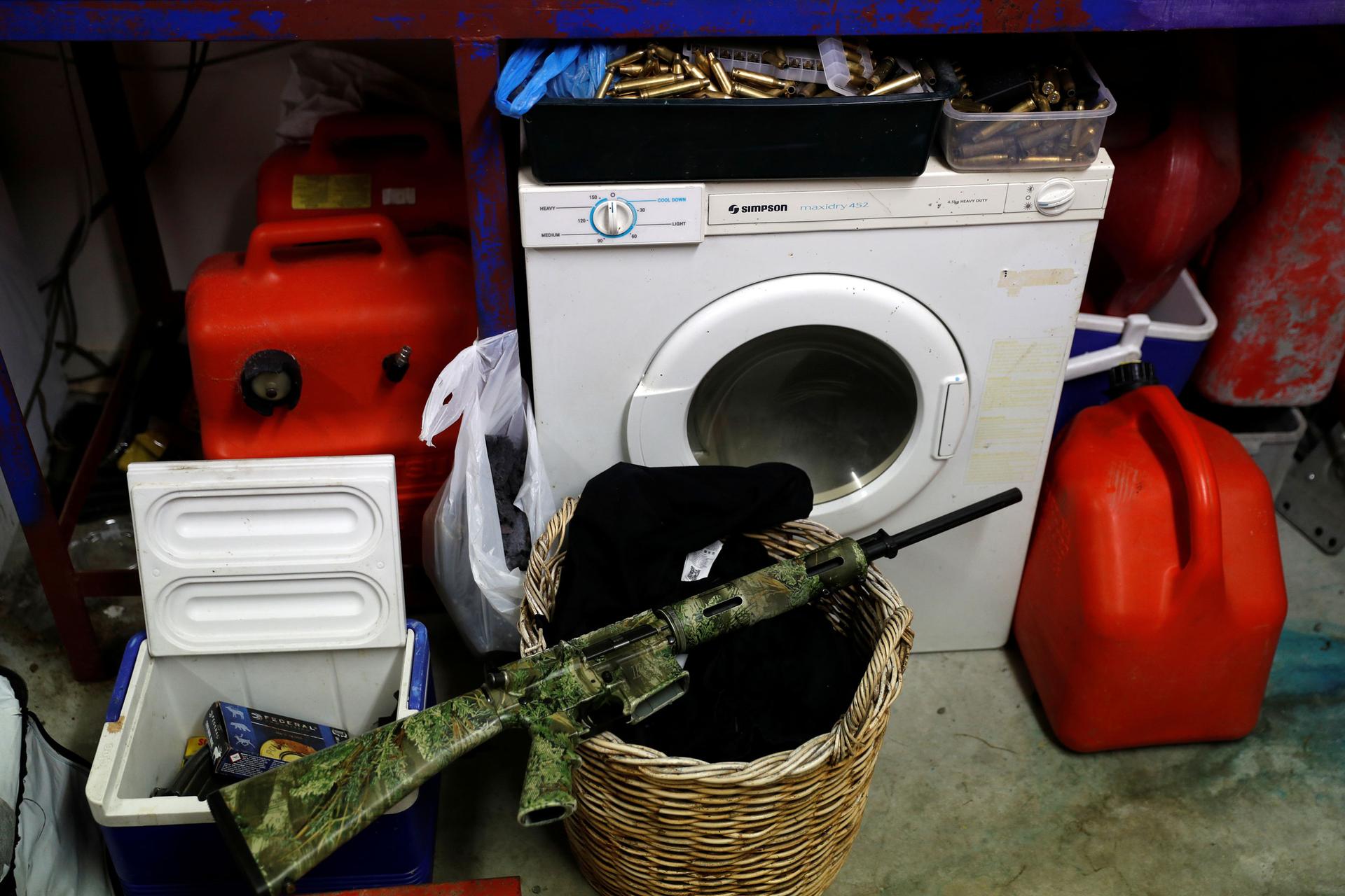An AR-15 semi-automatic rifle is seen painted in camoflage and sitting on a laundry basket.