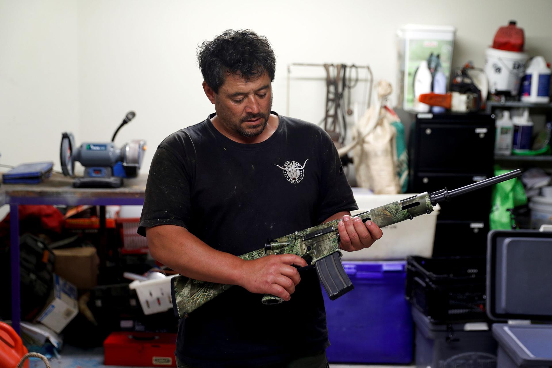 Noel Womersley is shown standing in a drak shirt holding his AR-15 semi-automatic rifle.
