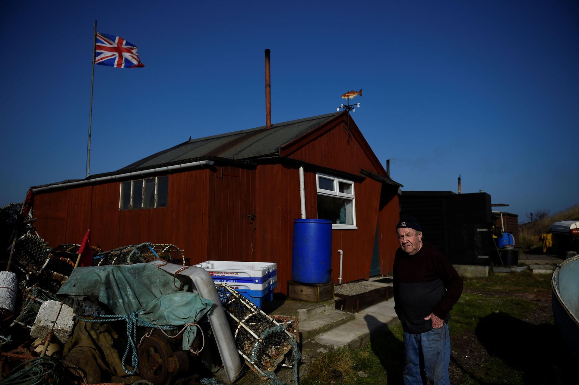 Mohan walks by a red, wooden fishing hut that has a British flag flying behind it.