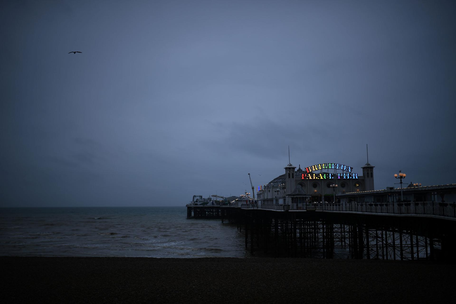 A large building is shown at the end of a pier with a sign illuminated with rainbow colors.