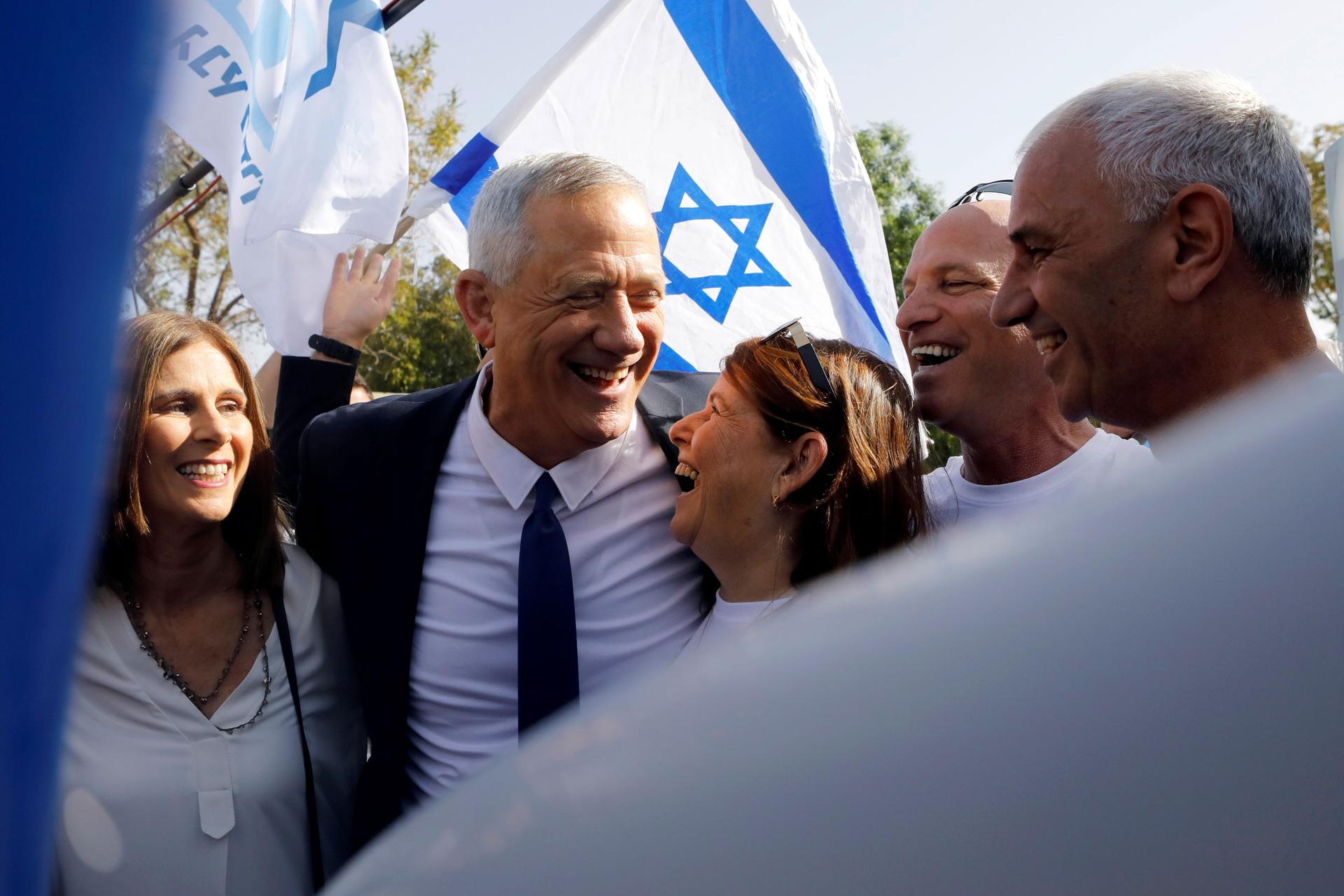 Benny Gantz is shown hugging his wife under his arm and an Israeli flag held behind him in the background.