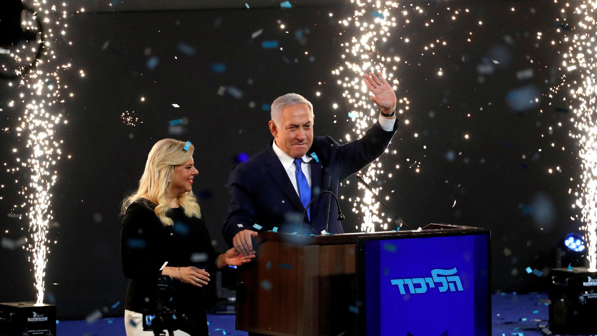 Confetti is shown falling falling with sparkling fireworks shooting up with Israeli Prime Minister Benjamin Netanyahu and his wife Sara standing on stage.