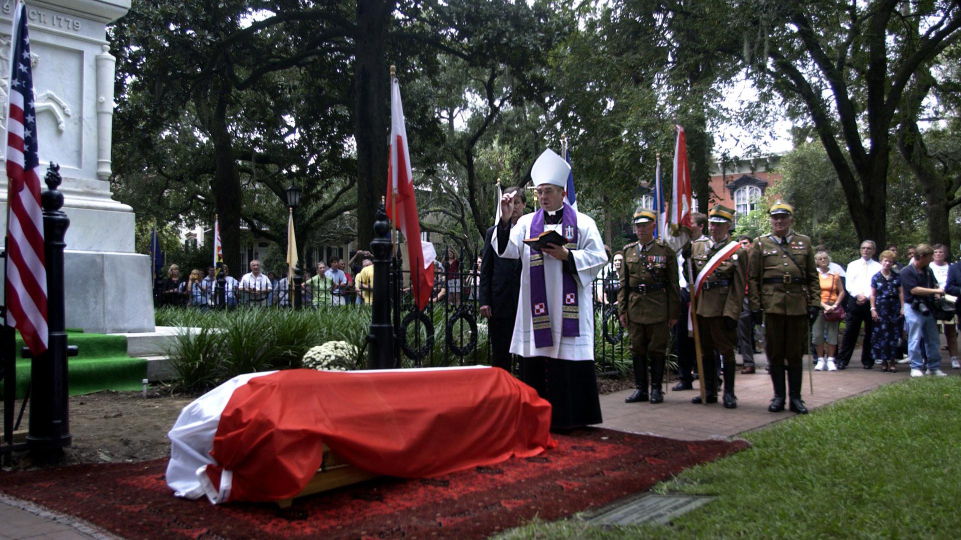 A bishop sprinkles holy water on a coffin covered in the Polish flag